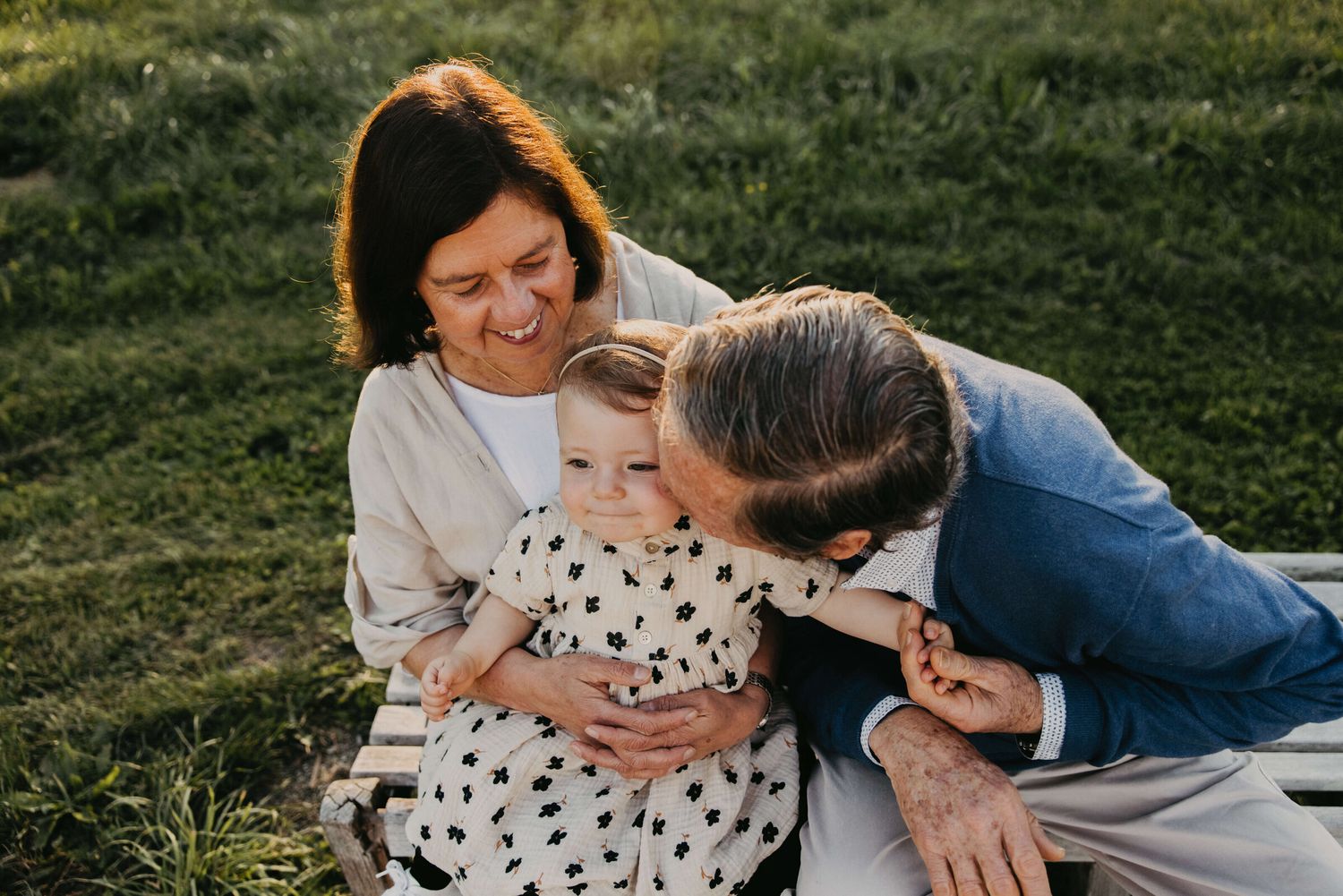 Family sharing tender moments on grassy field during sunset photo session.