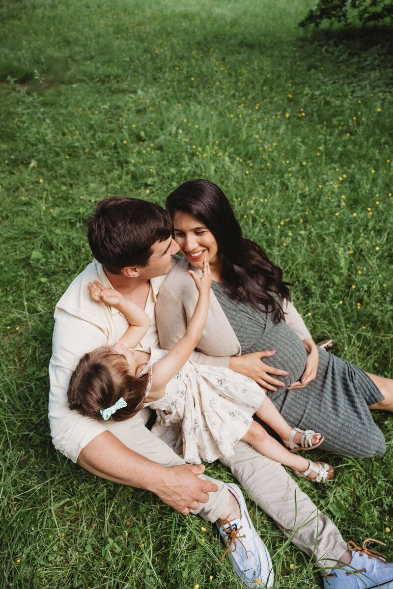 A couple lying on grass together in casual attire during an intimate outdoor photoshoot.