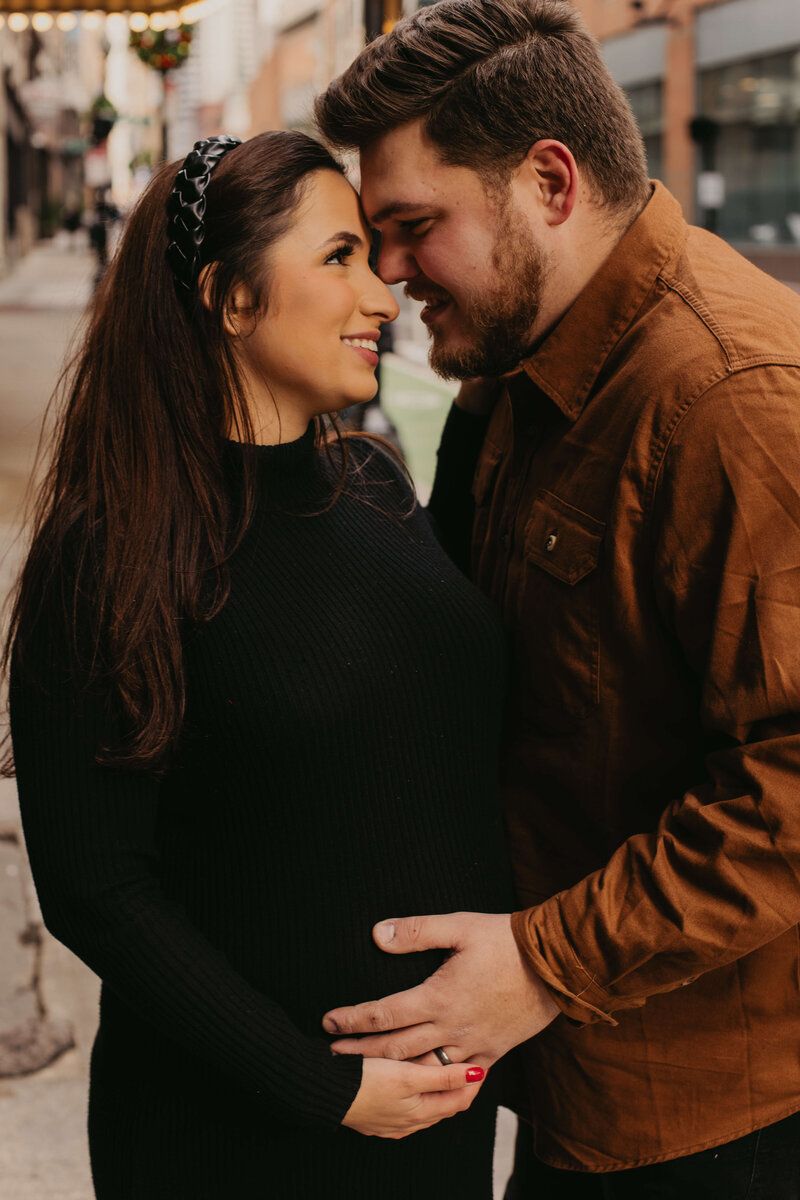 Romantic couple sharing tender moments in brown and black outfits against urban backdrop.