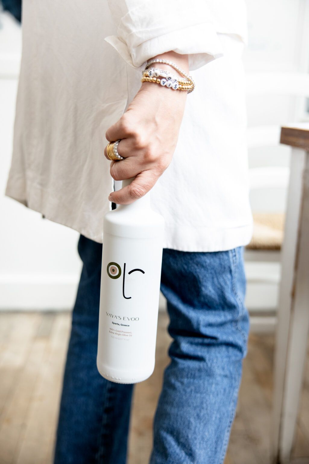 Person in blue jeans holds a minimalist white bottle with simple black logo design against light background.