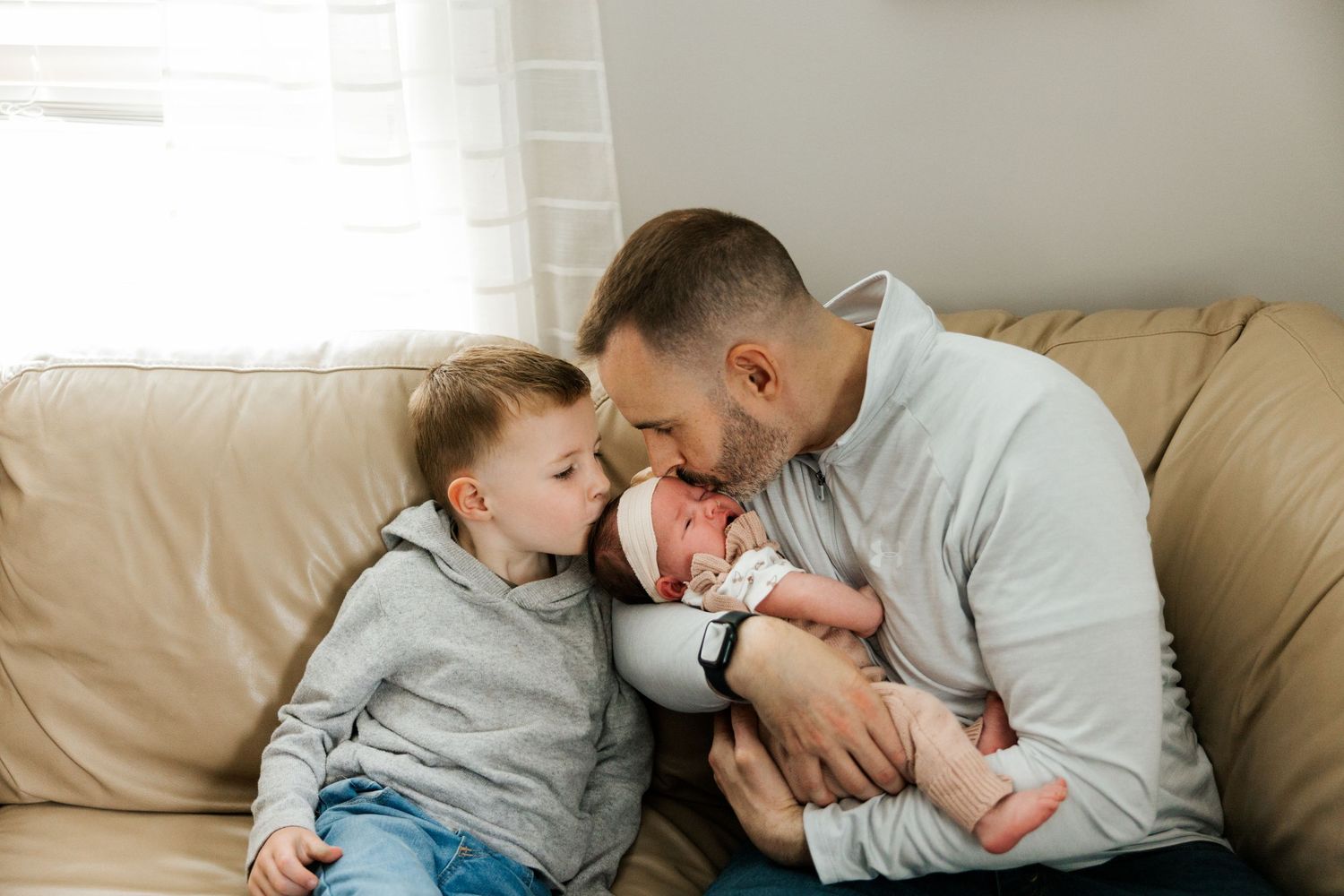 A tender family moment shared on a beige couch as they snuggle close together at home.