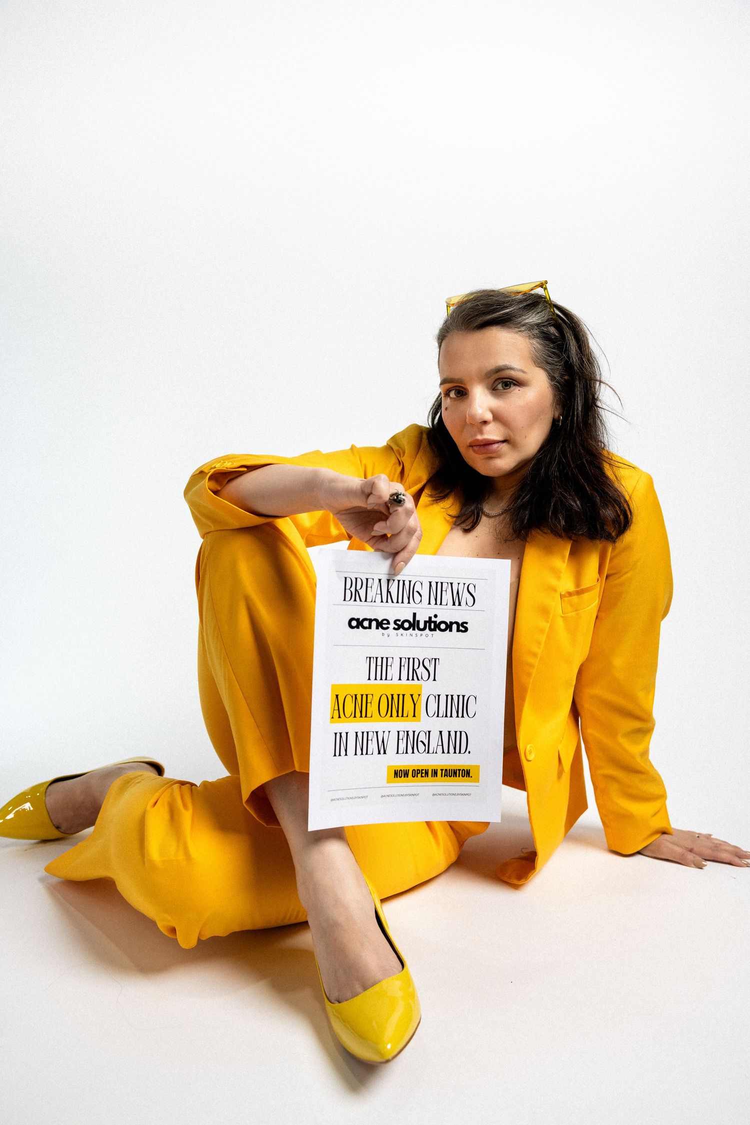 Person in yellow outfit lying on white background displaying book covers in artistic photoshoot.