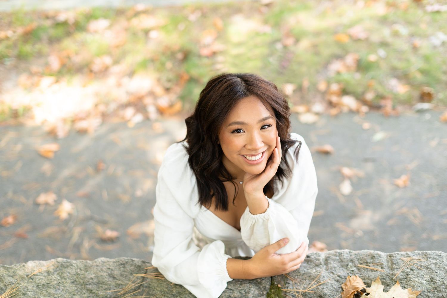 A series of five outdoor portraits showing someone in a white top sitting and posing among autumn leaves.