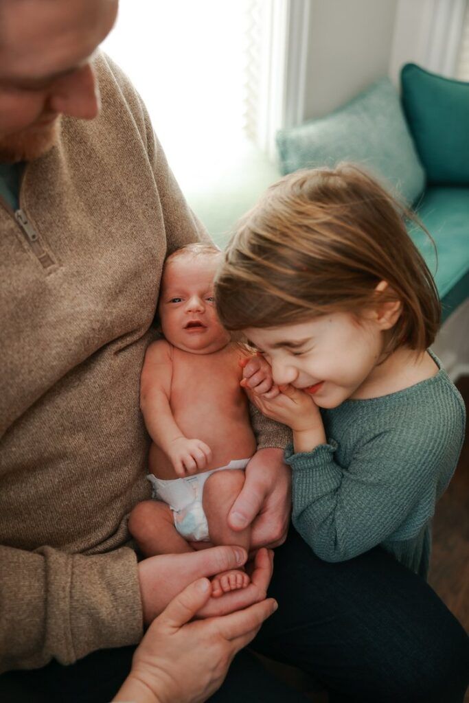 Siblings share tender loving kisses with a newborn baby while sitting on a cozy couch.