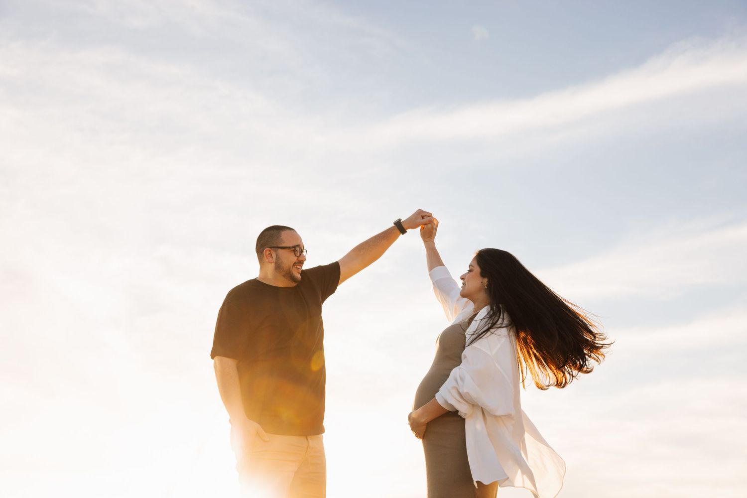Couple dancing and twirling during golden hour on waterfront.