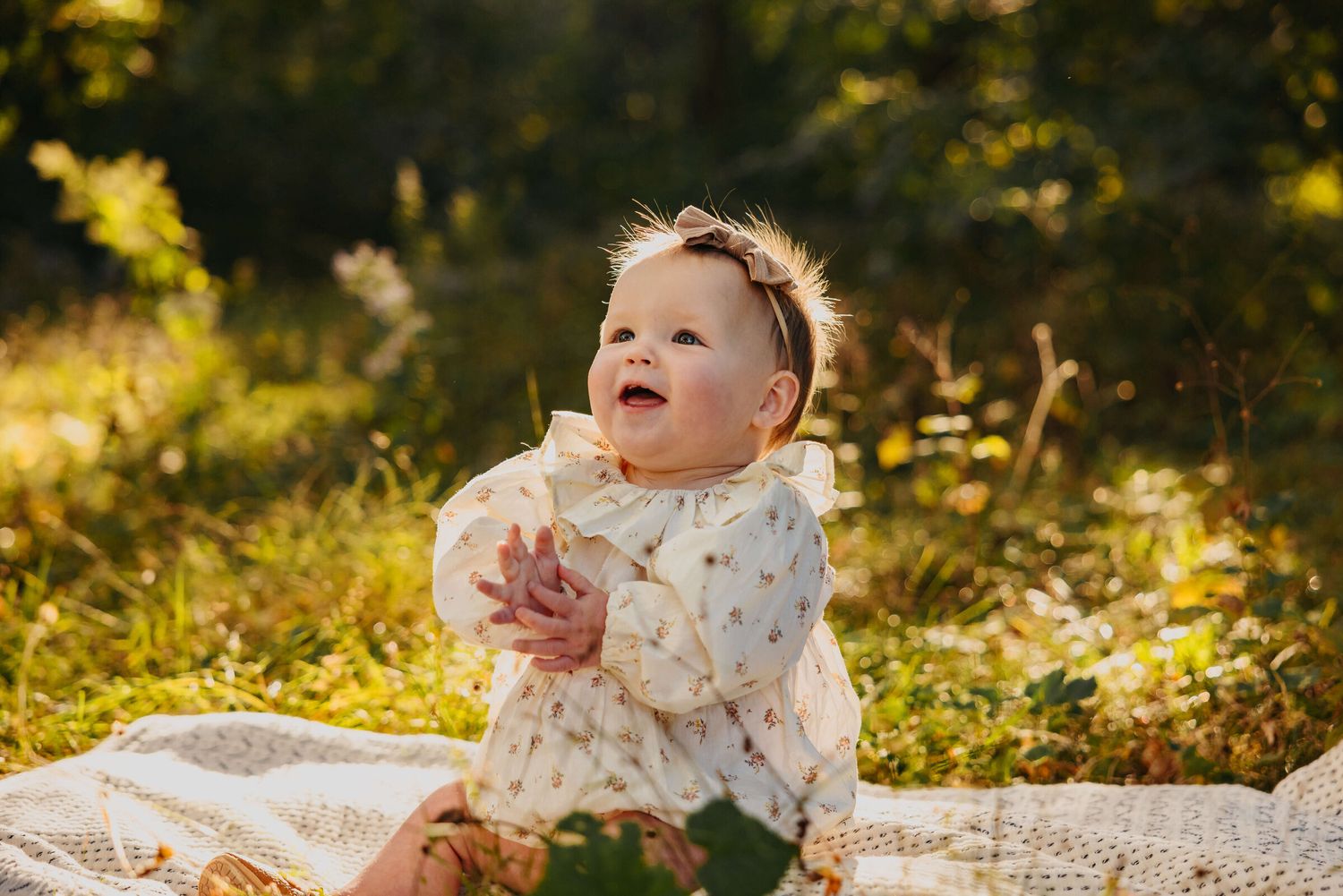 Baby in white dress laying on blanket during golden hour outdoor photo session.