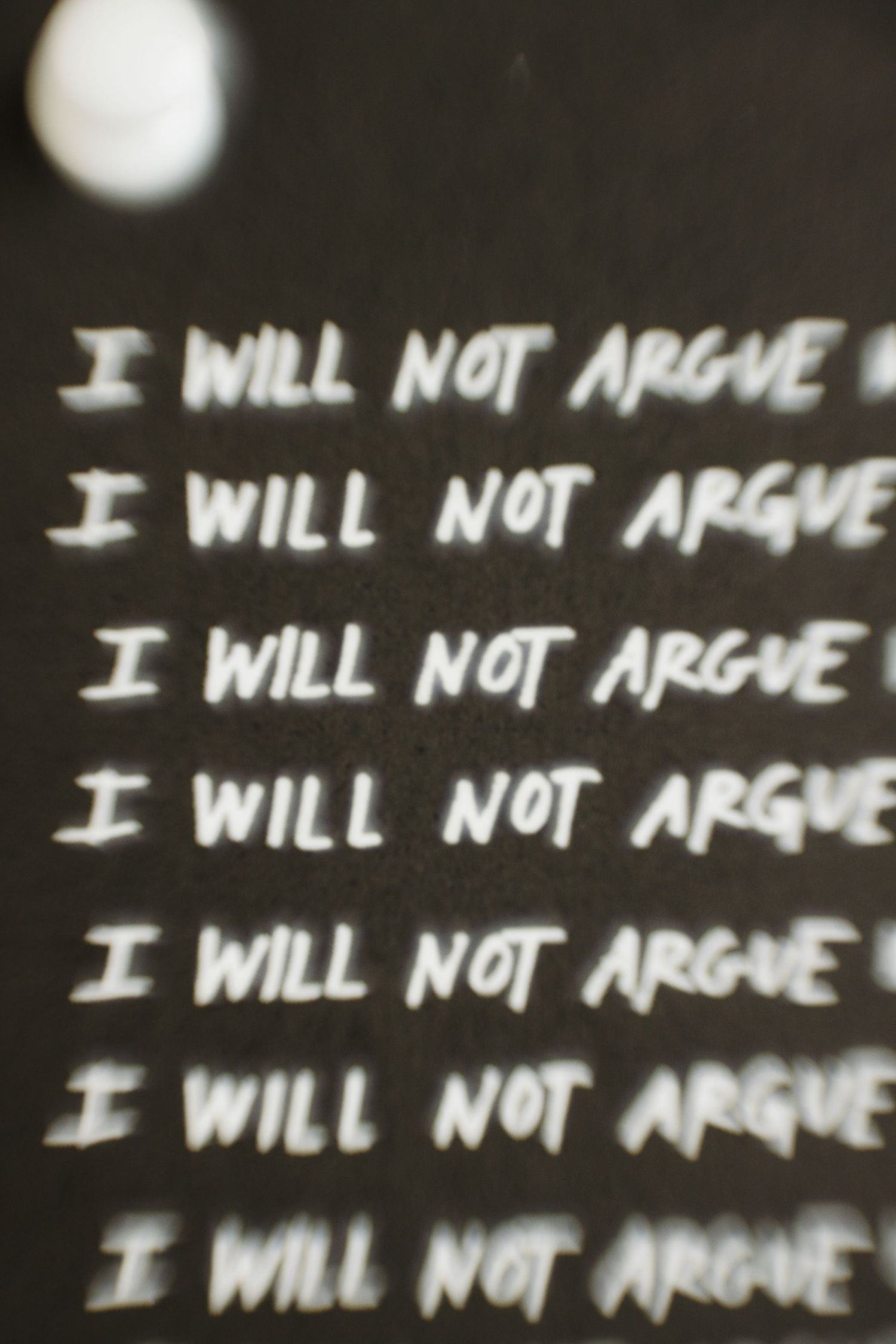 A chalkboard displays repeated handwritten text reading 'I WILL NOT ARGUE' in white chalk against a dark background.