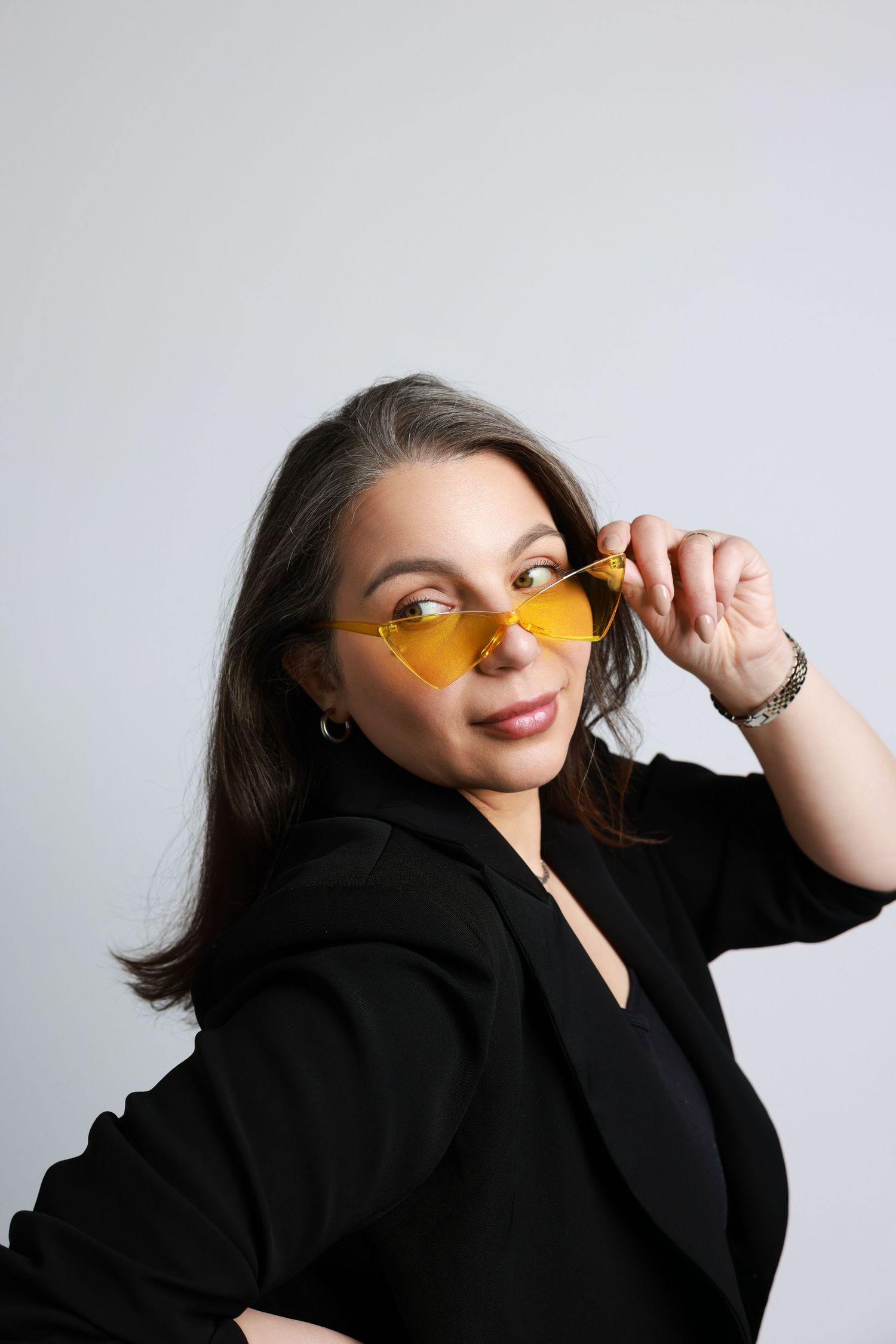 Person in black blazer strikes poses with yellow-tinted sunglasses in studio photoshoot series.