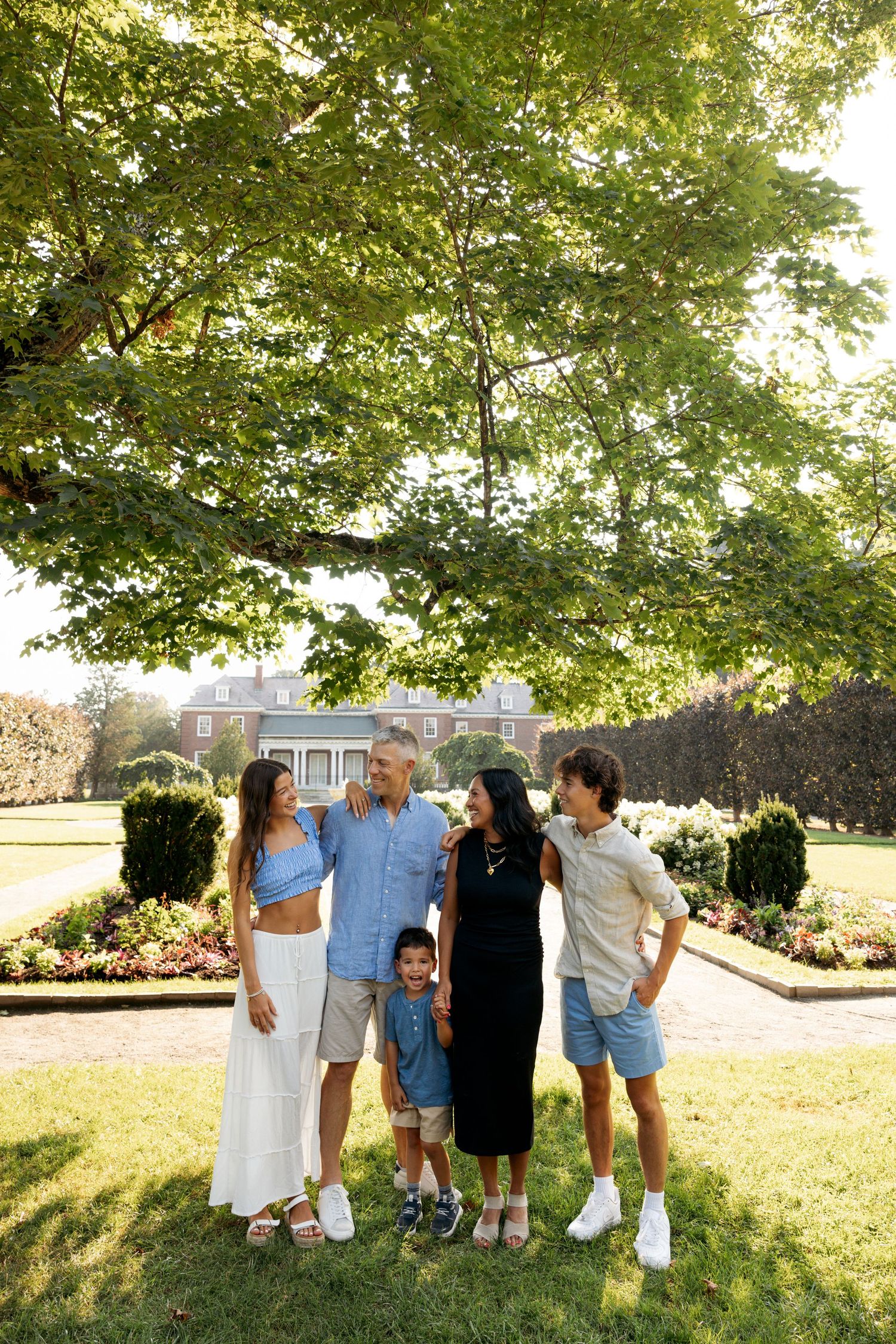 Group stands together outdoors on grass underneath green leafy trees for a casual photo.