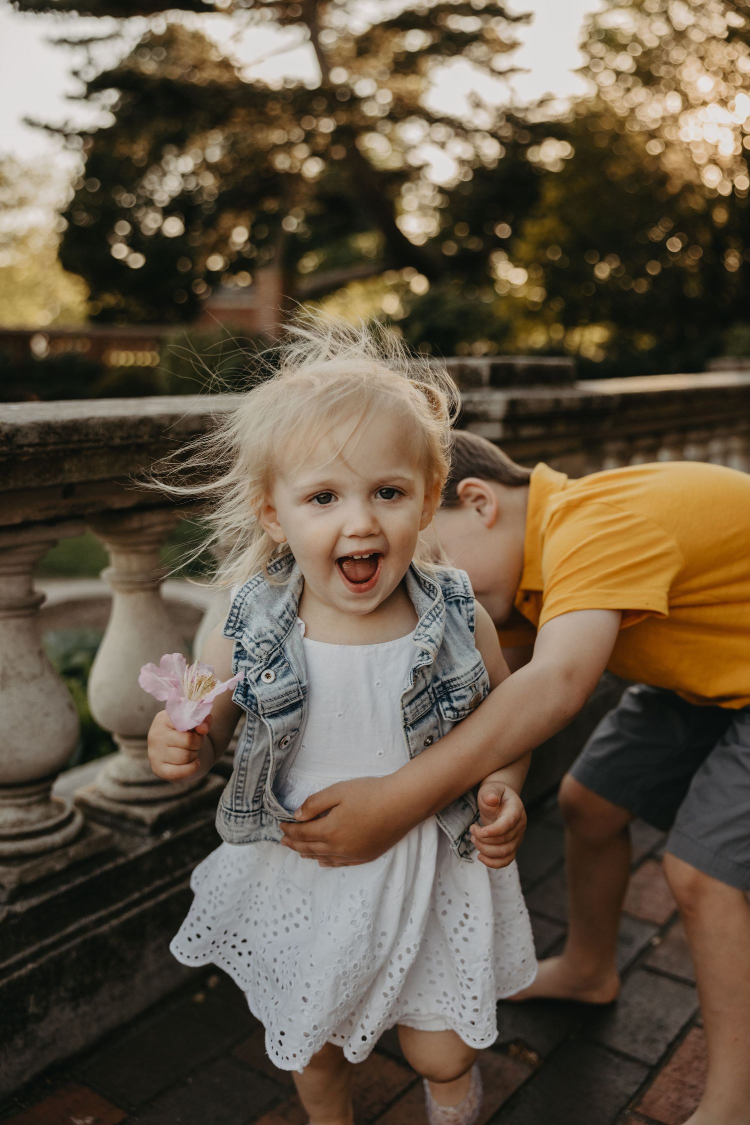 Child in a white dress laughs during playtime outdoors at sunset.