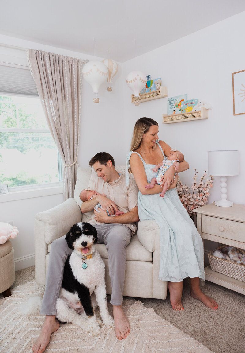 Family relaxes in nursery with black and white dog on plush carpet.