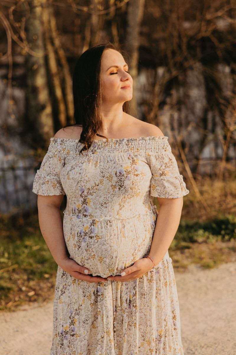 Woman in floral dress poses outdoors in natural lighting.