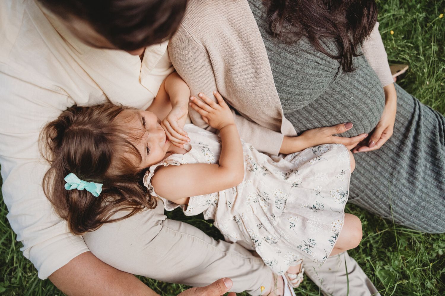 Tender moment of parent and child relaxing on a blanket outdoors in white and floral dress outfits.