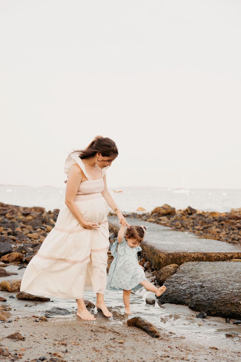 Mother and child exploring rocky beach together at sunset.