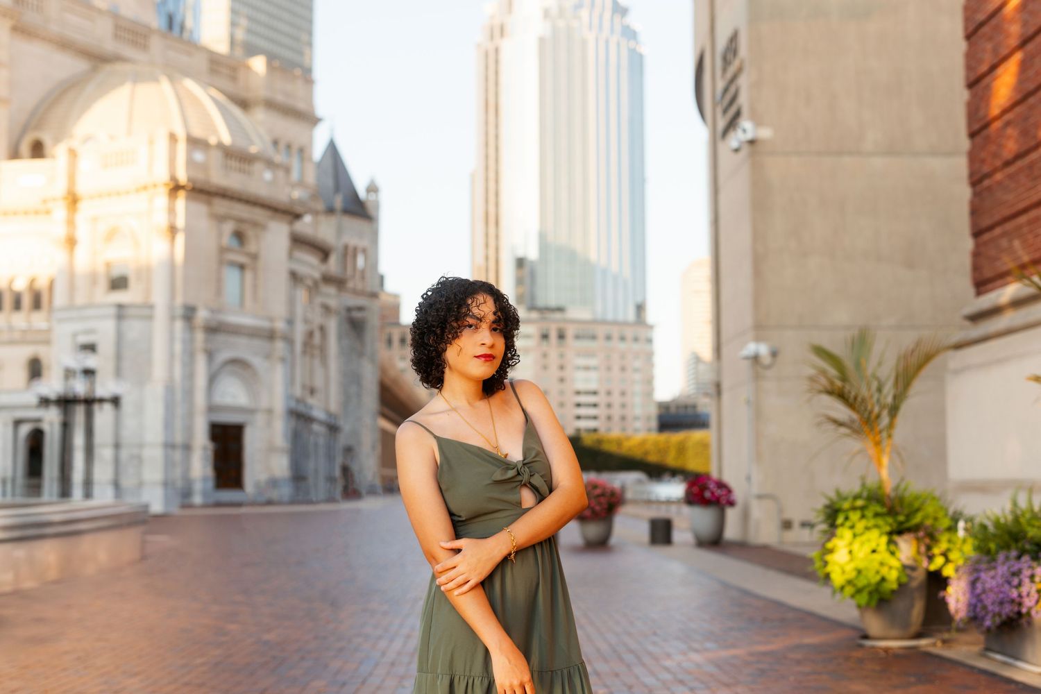 Woman in black dress poses elegantly on a grand staircase with ornate architecture and city buildings in background.