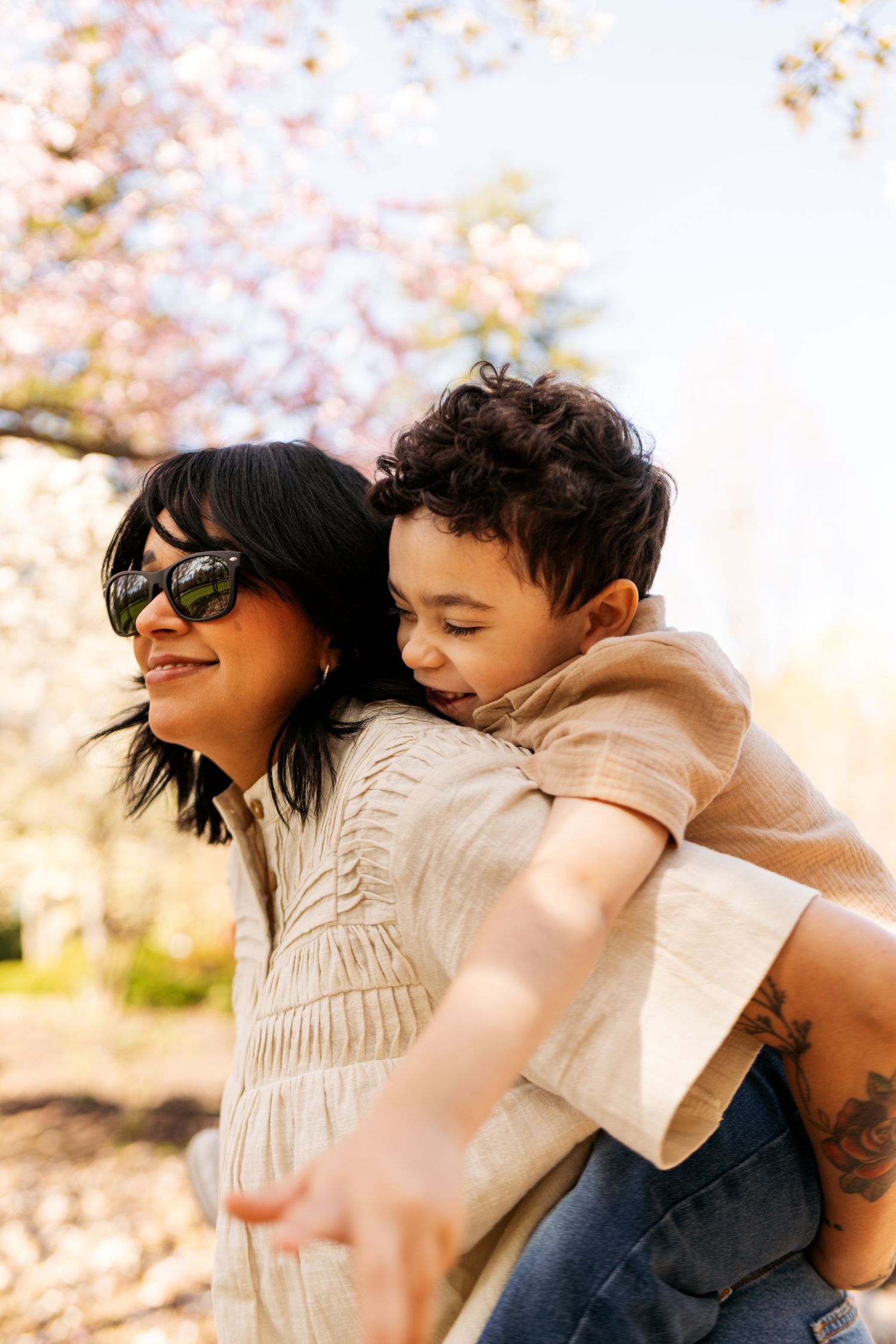A joyful springtime piggyback ride outdoors with cherry blossoms blooming in the soft sunlit background.