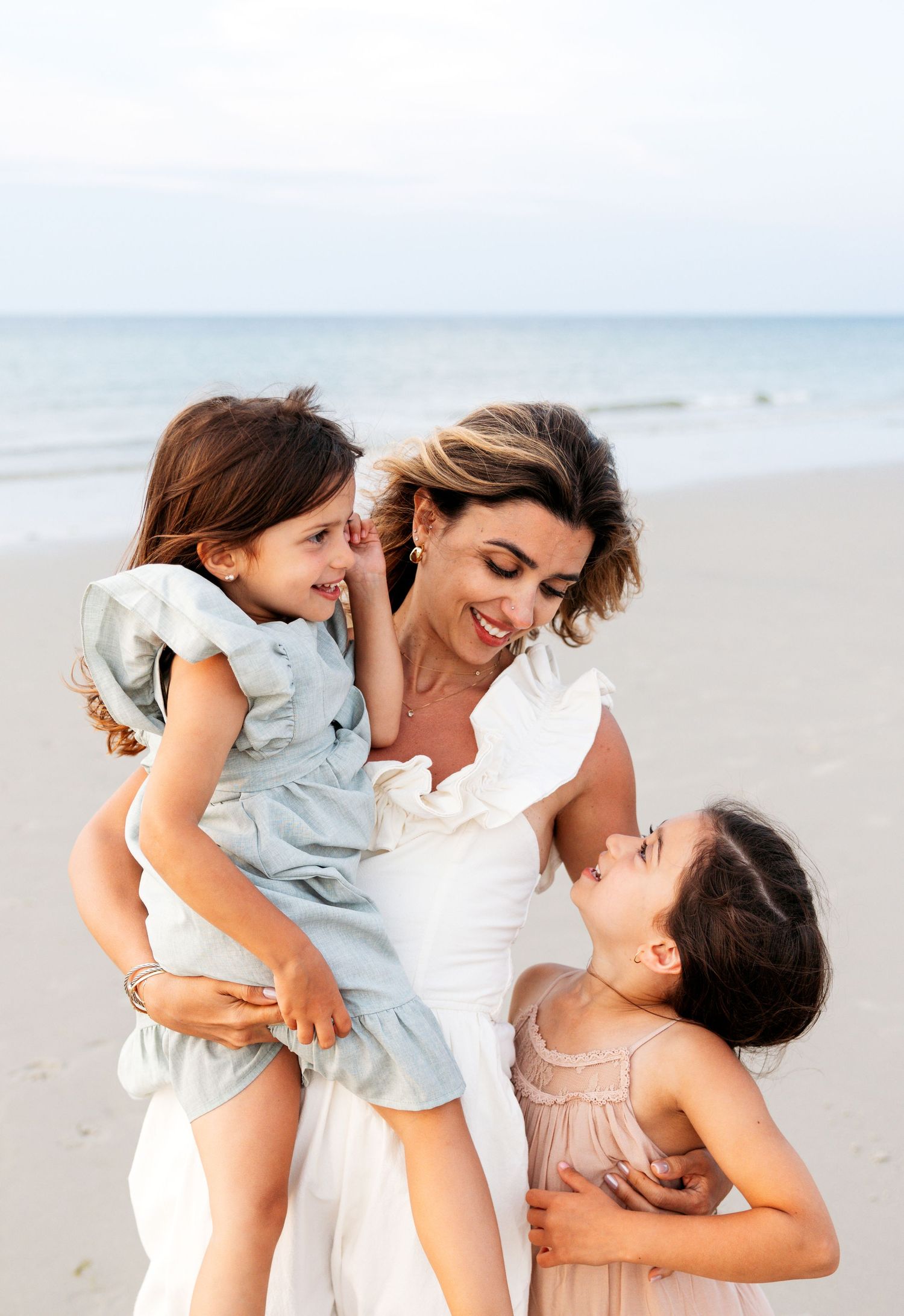 A joyful family moment captured in soft light on the beach with gentle embraces and laughter shared between them.