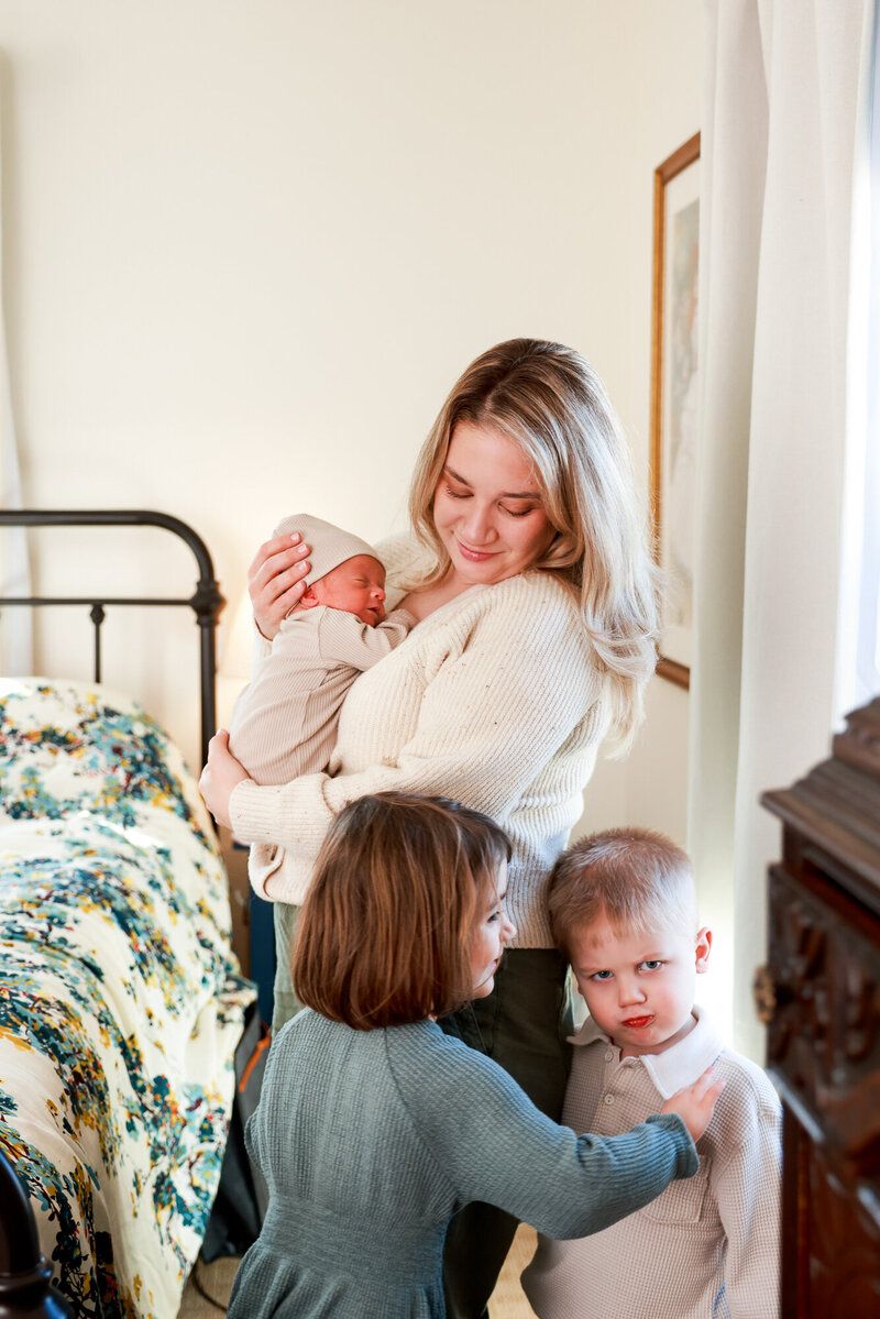 Family members share a tender moment with newborn baby in bedroom with vintage bed and floral bedding.