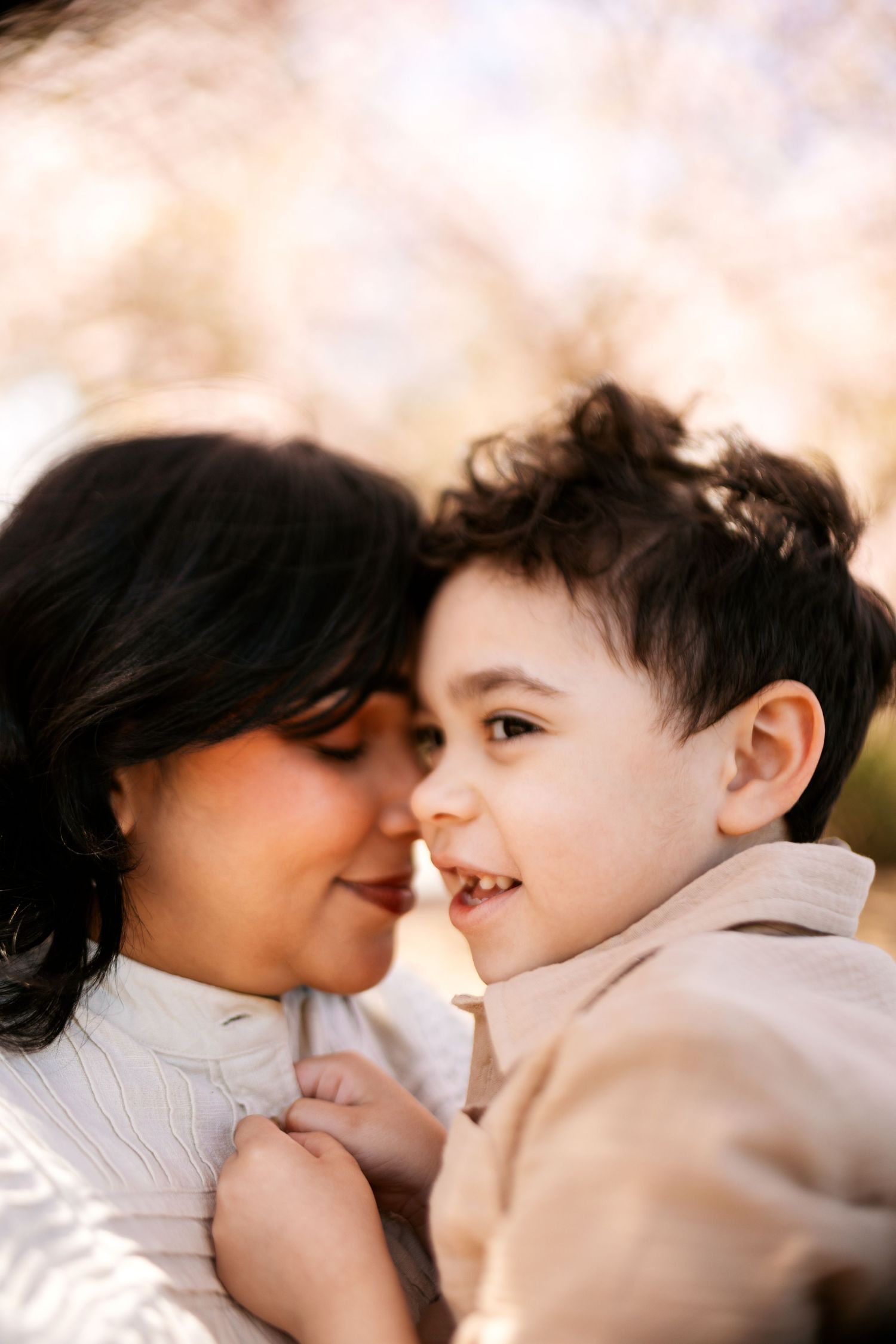 Sweet candid moment between parent and child as they share loving glances surrounded by spring blossoms.