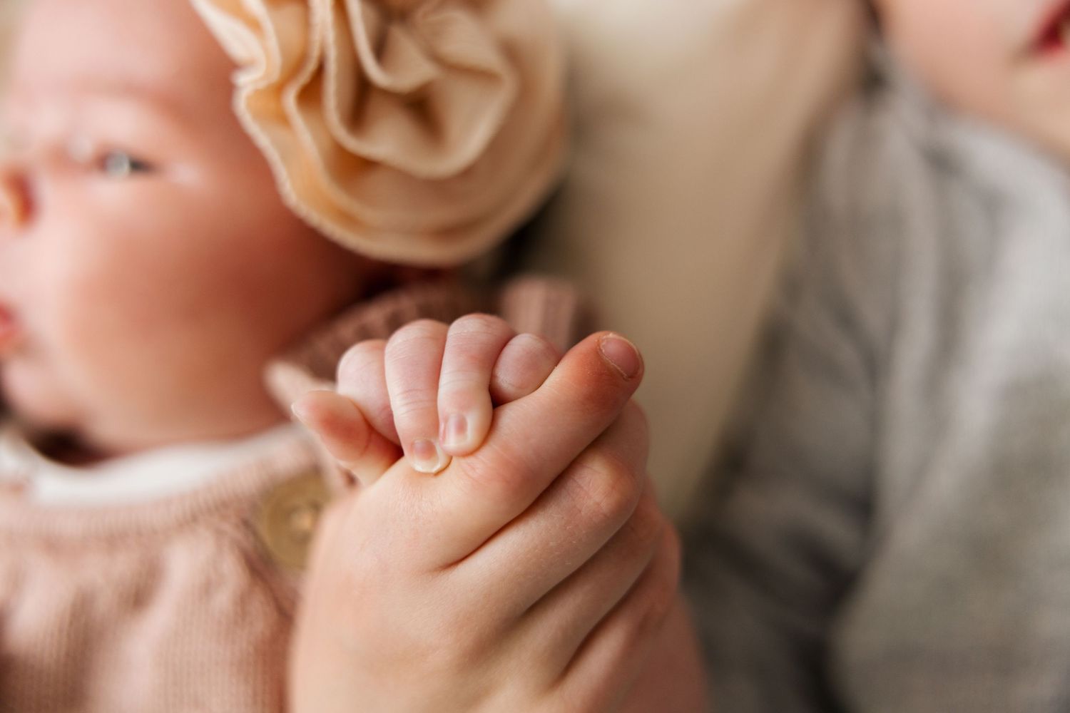 Close-up view of baby hands with soft pink skin tones, showing delicate fingers against a blurred light background.
