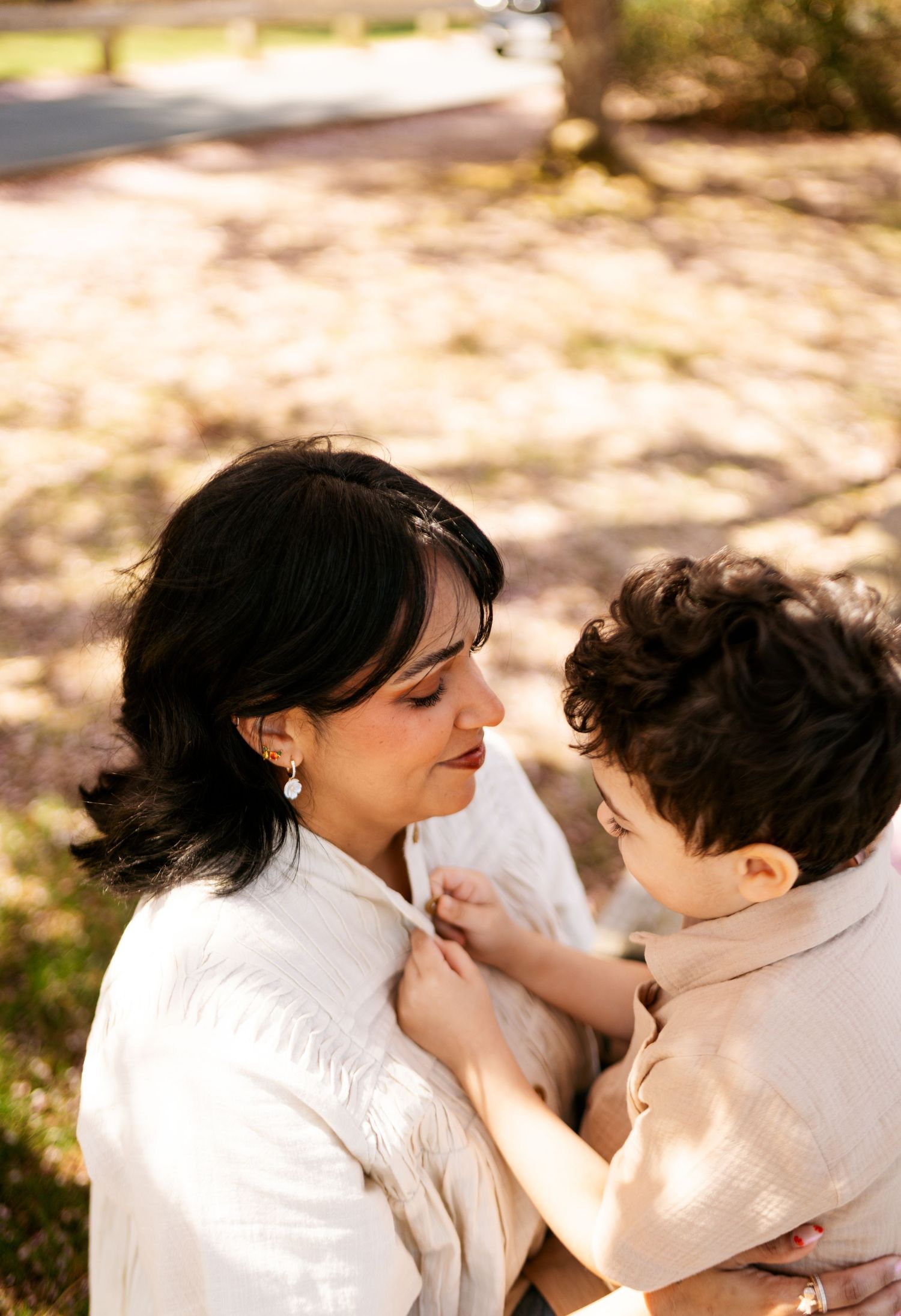 A tender moment captured between parent and child wearing white outfits in warm sunlit outdoor setting.