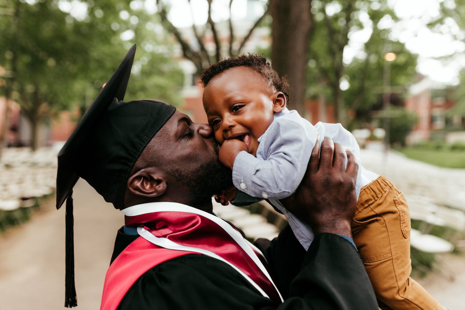 Sweet embrace captured in front of brick buildings during graduation ceremony.