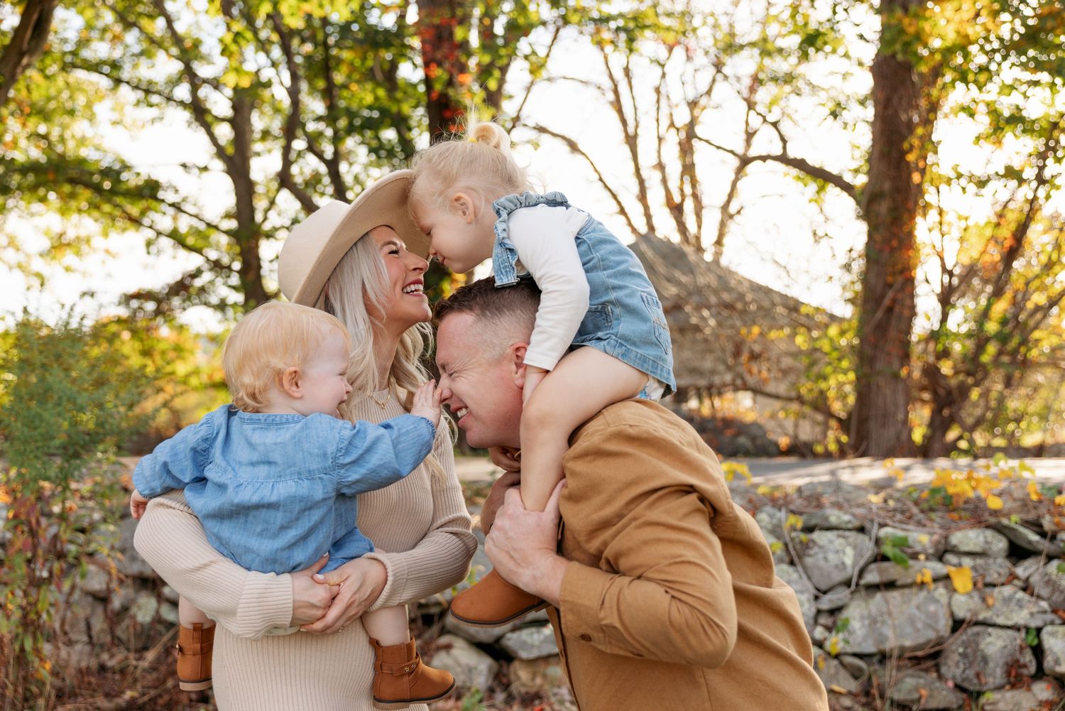 Family cuddles together on stone wall during golden autumn afternoon.