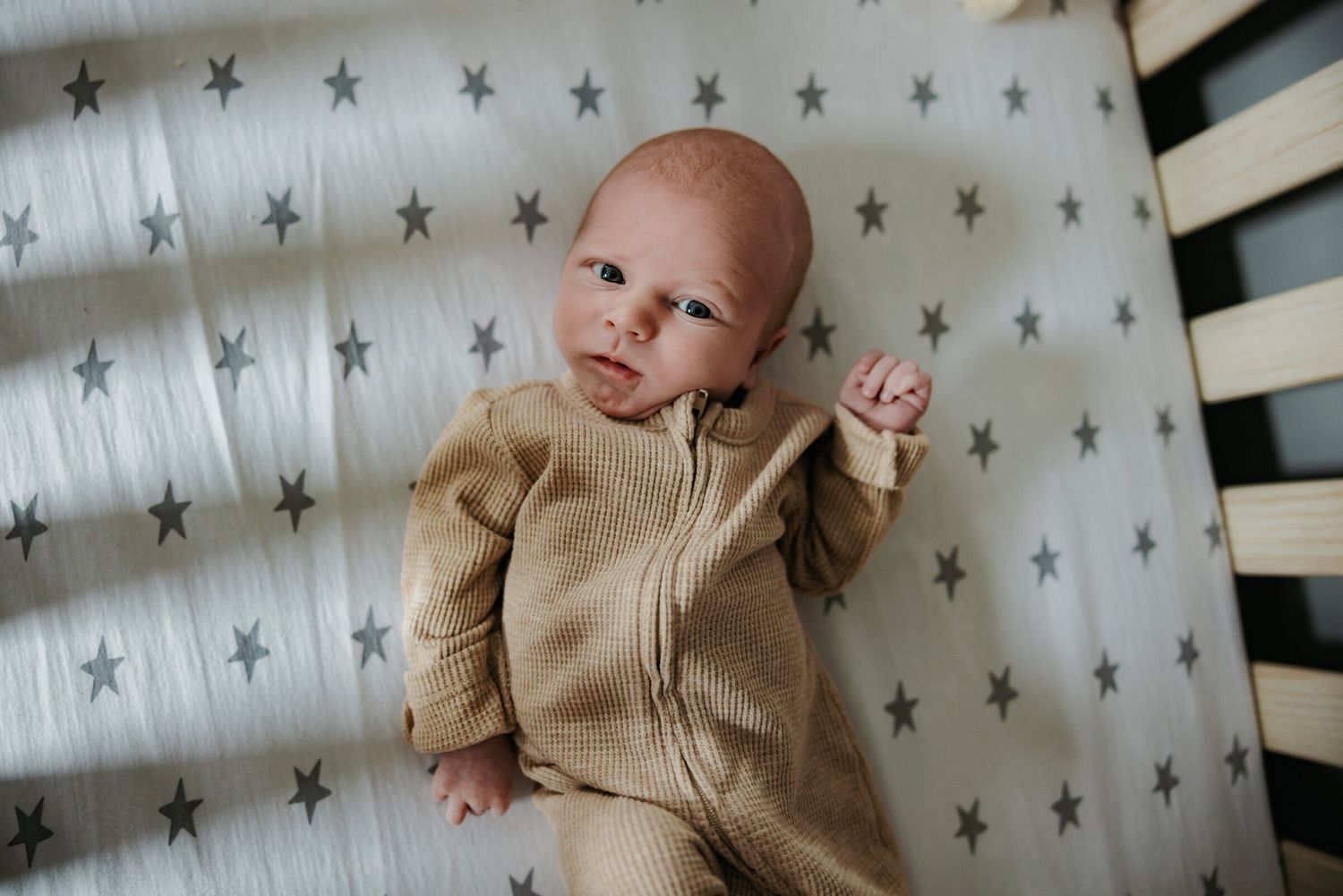 Baby in tan onesie lying on star-patterned crib sheets.