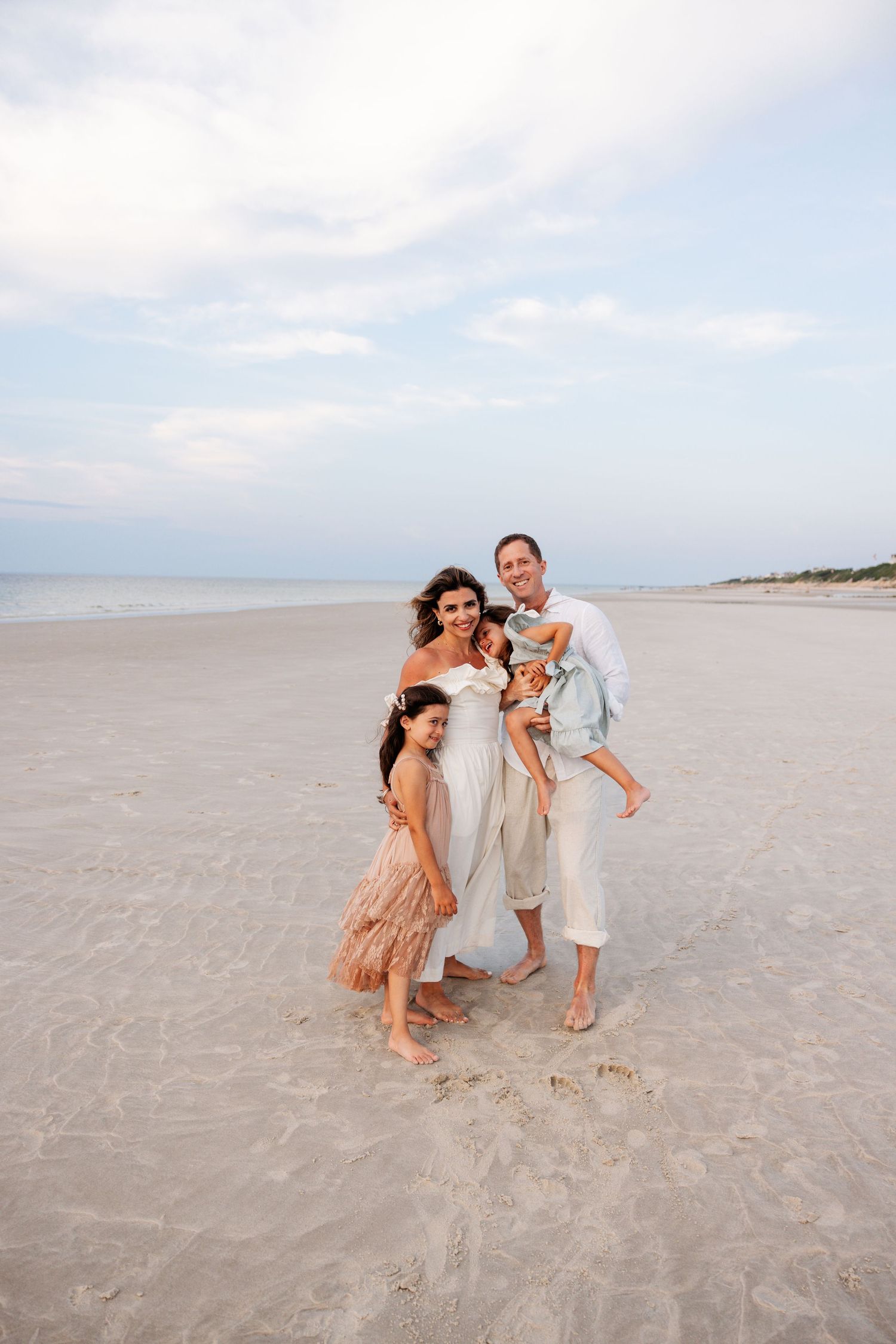 Three people in coordinating outfits play and laugh together on a peaceful sandy beach at sunset.