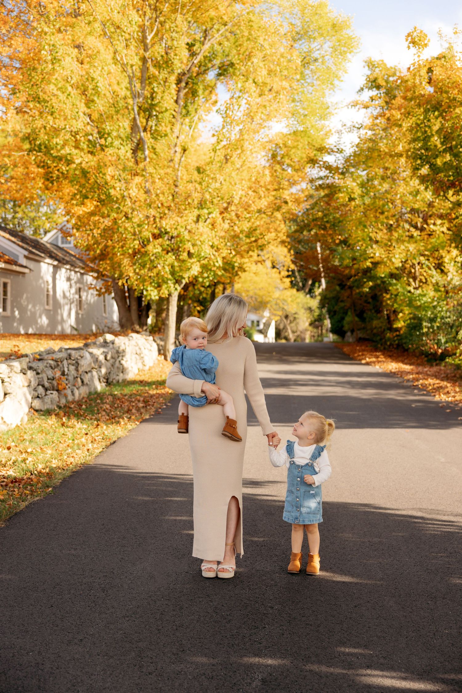 Small children walk hand in hand down a street lined with golden autumn trees.