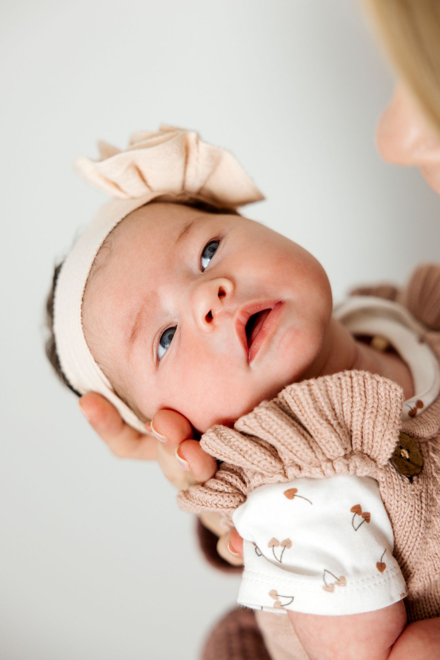 Series of close up images showing a baby in a pink knit outfit looking up with bright eyes and sweet expressions.