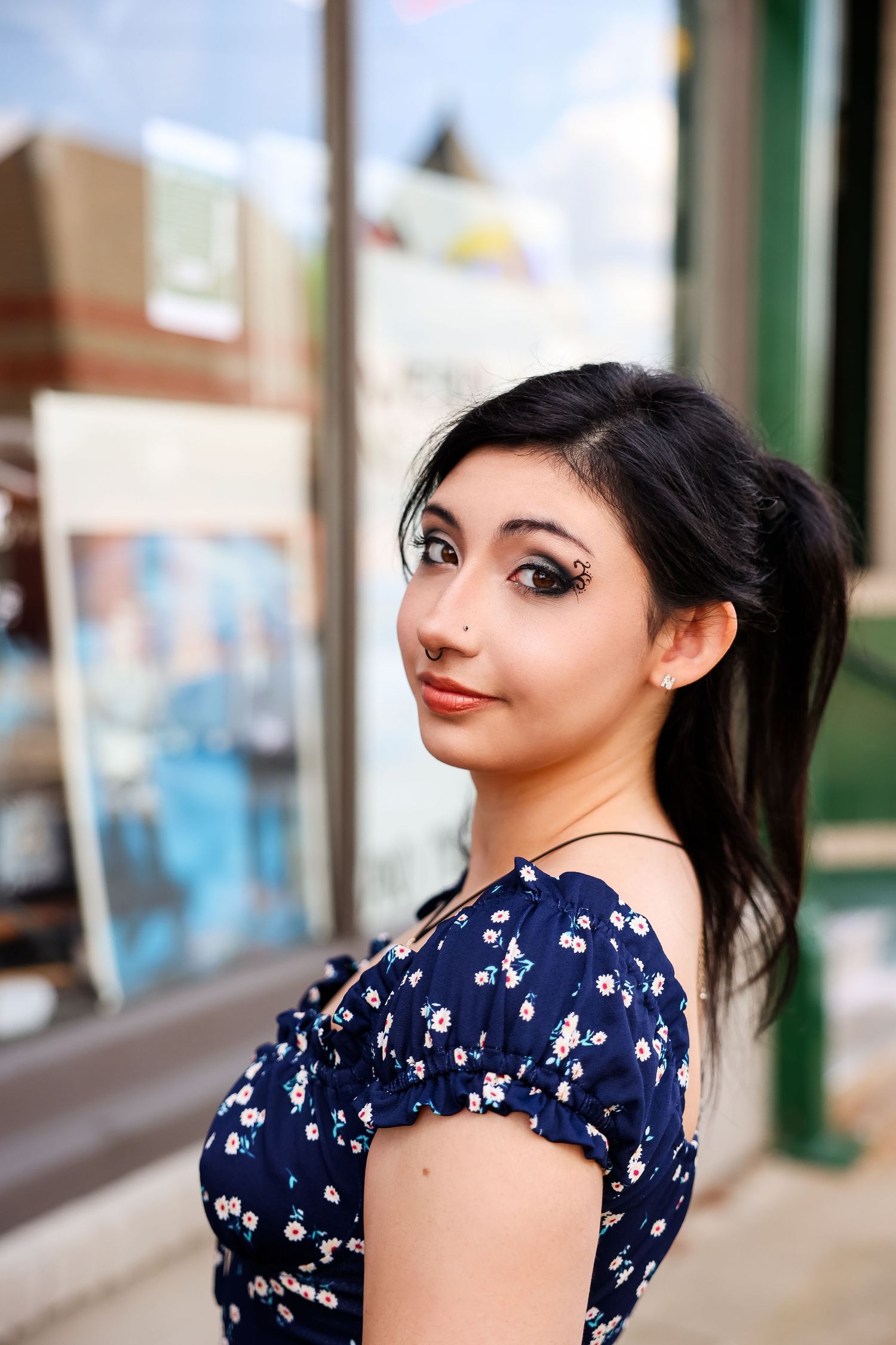 Portrait of someone in a navy floral dress with puff sleeves posing against an urban storefront background.