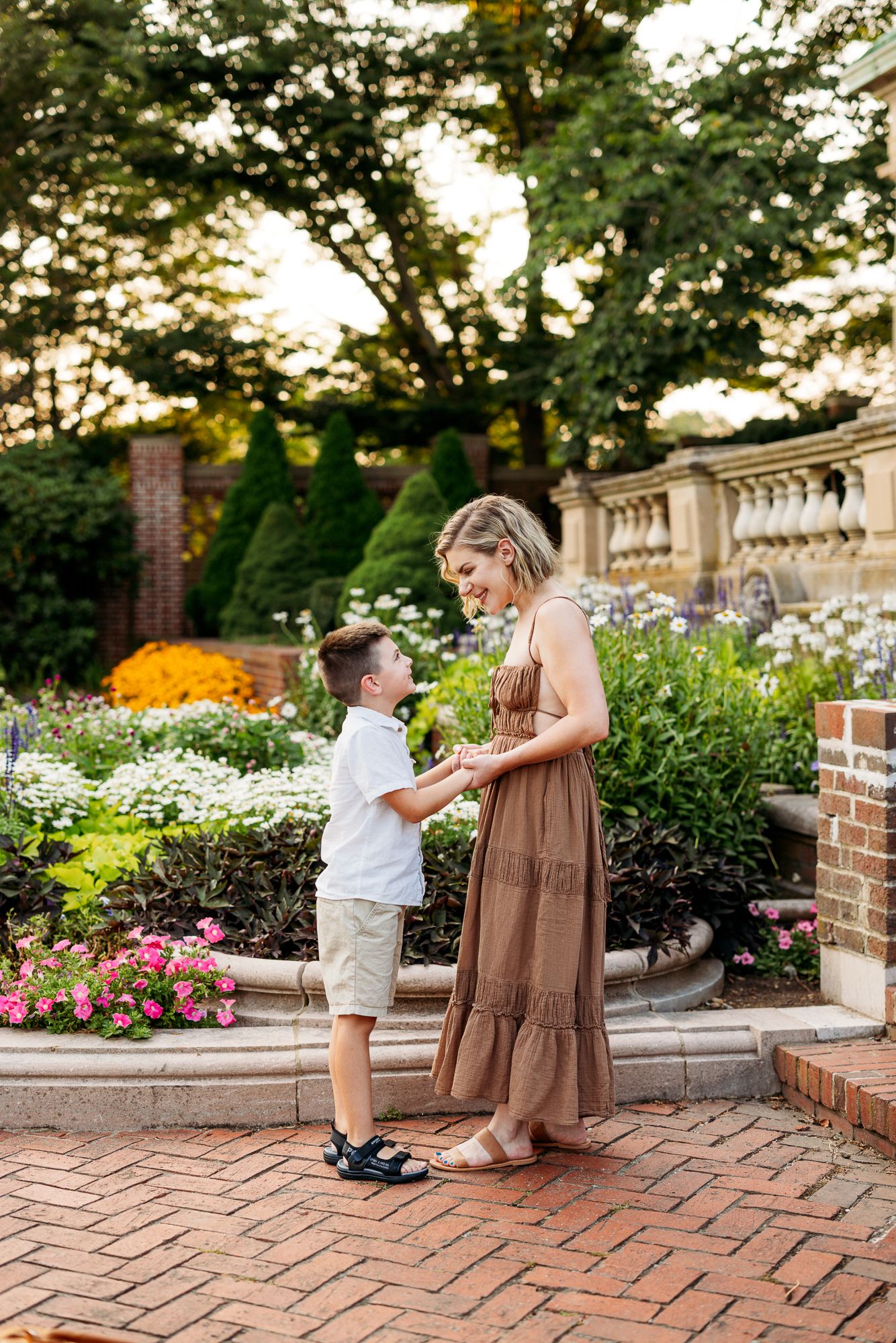 Couple shares a tender moment on brick patio surrounded by blooming garden flowers at dusk.