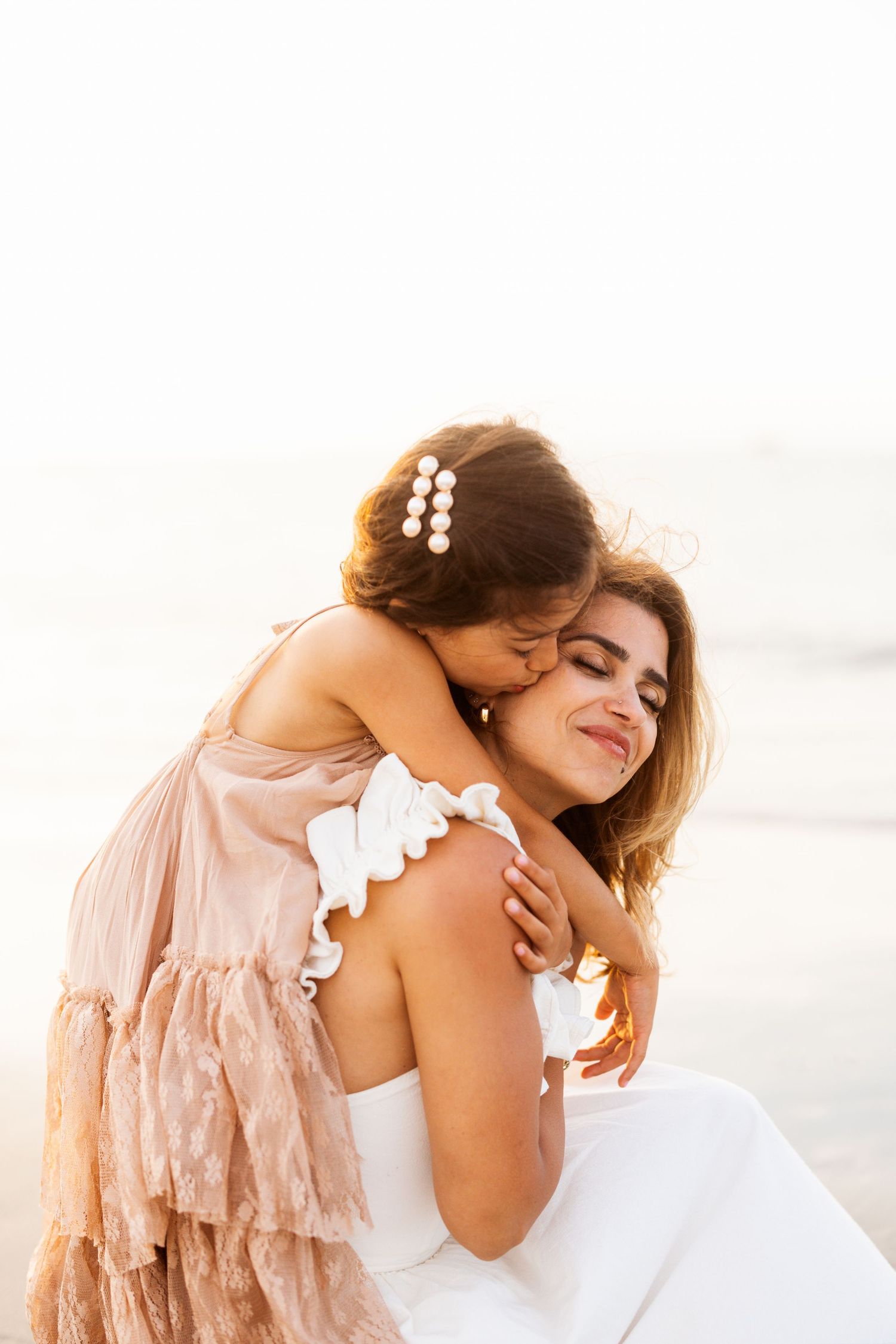 A tender embrace between parent and child wearing soft pink ruffled dress against a light background.