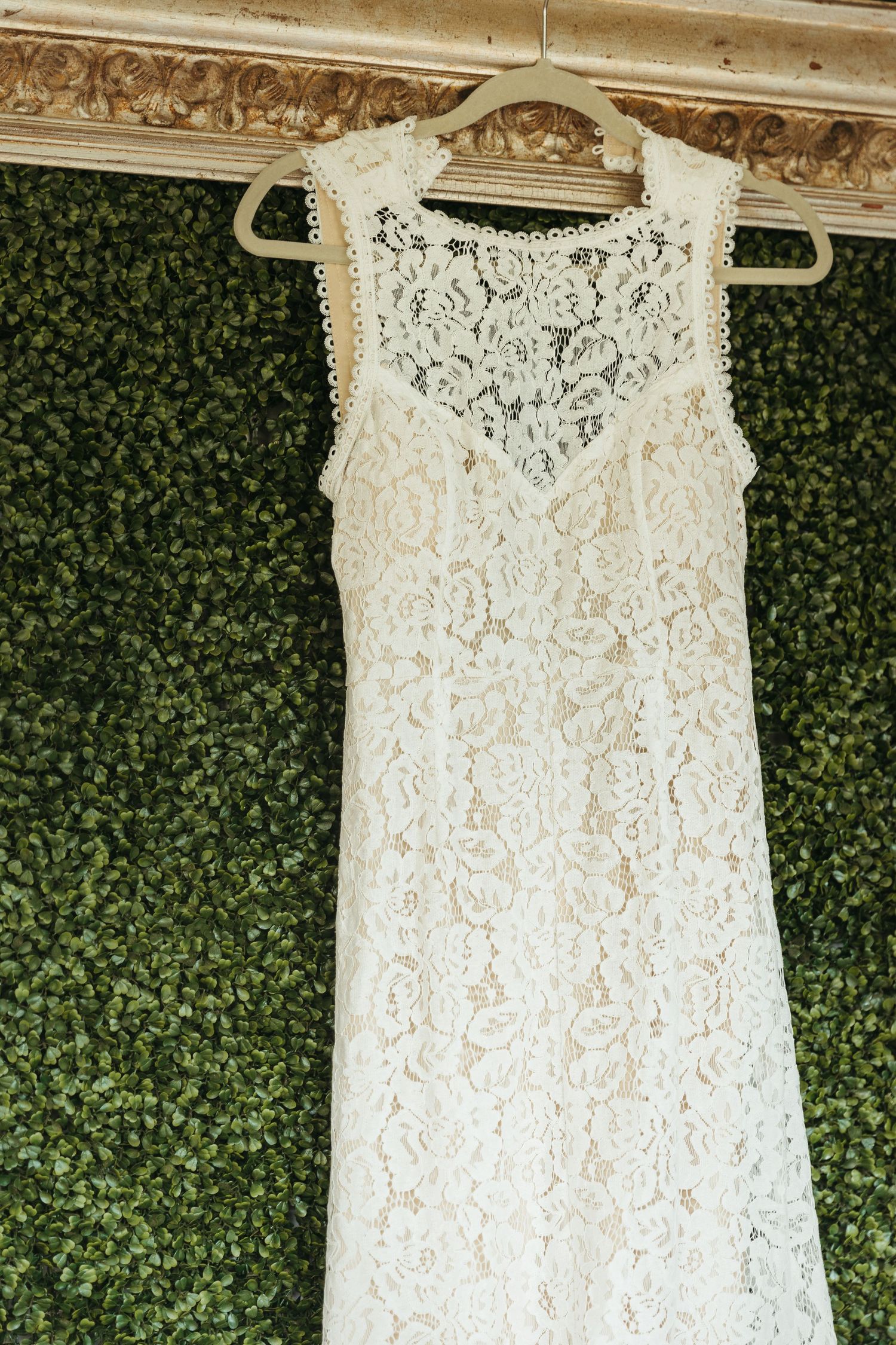 Close-up views of delicate white lace wedding dress details hanging against a green foliage backdrop.