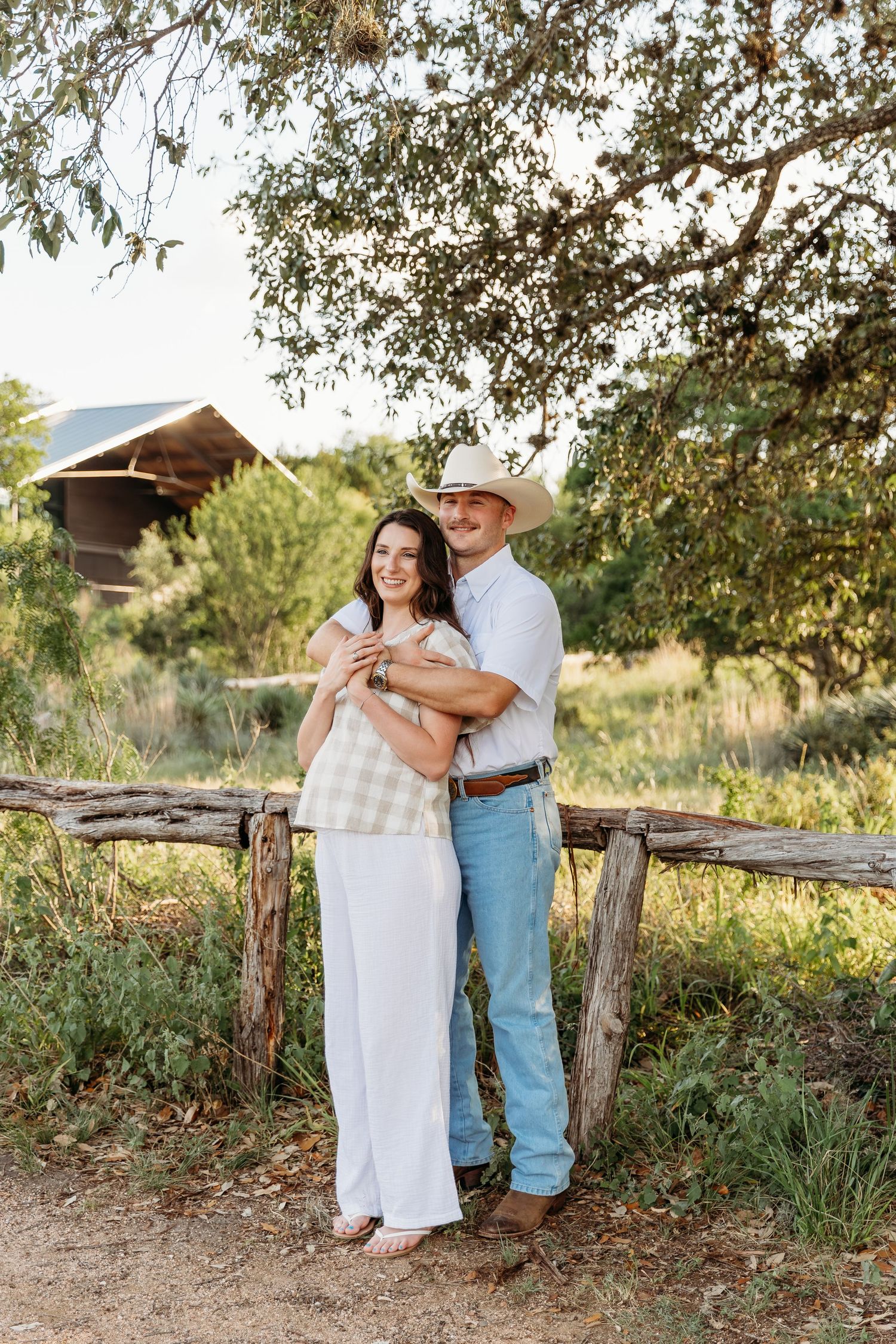 A couple in white and denim embrace and laugh together during a sunset photoshoot outdoors.