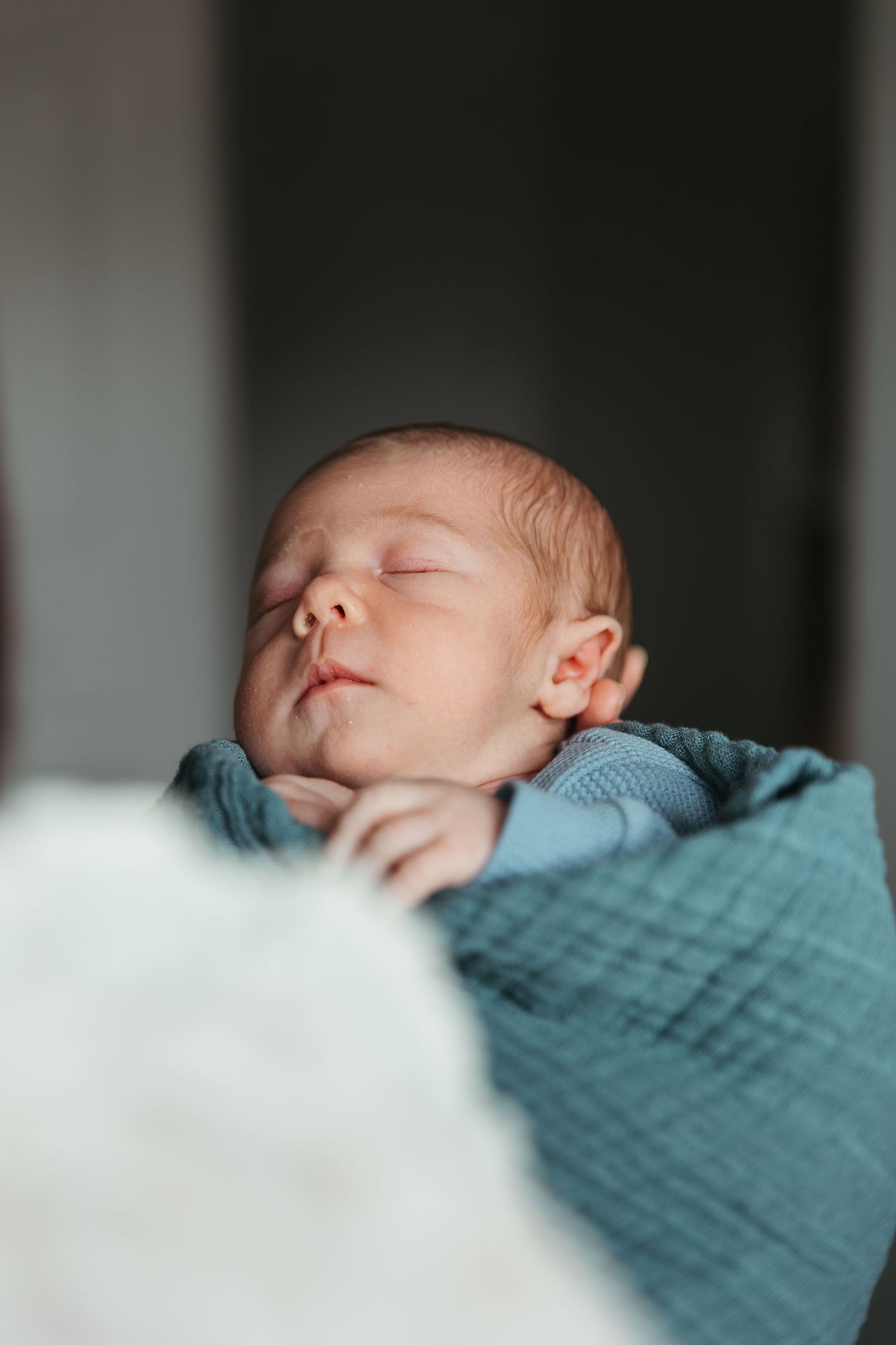 Peaceful sleeping newborn baby wrapped in soft blue blanket shown in close-up profile view.