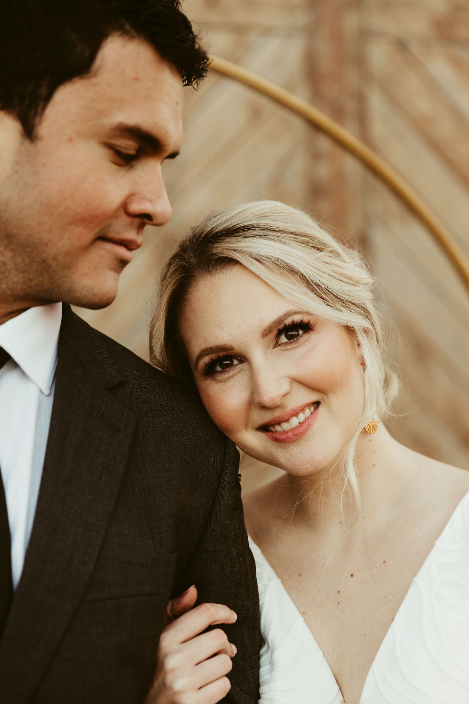 A romantic moment between newlyweds in front of a rustic wooden barn wall with floral decorations.
