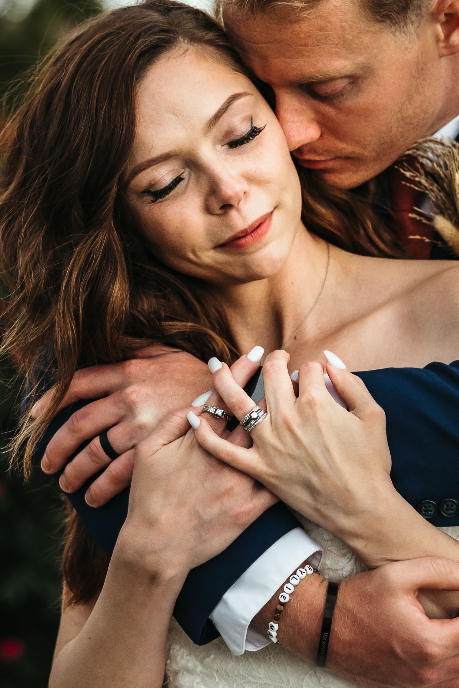 Romantic close-up portrait of couple embracing outdoors with hands clasped showing engagement ring.