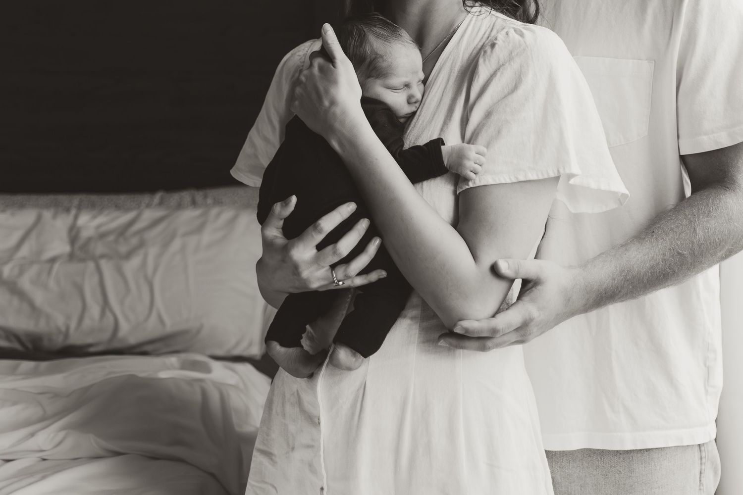 A black and white photo of a mother holding her newborn baby while the father hugs her
