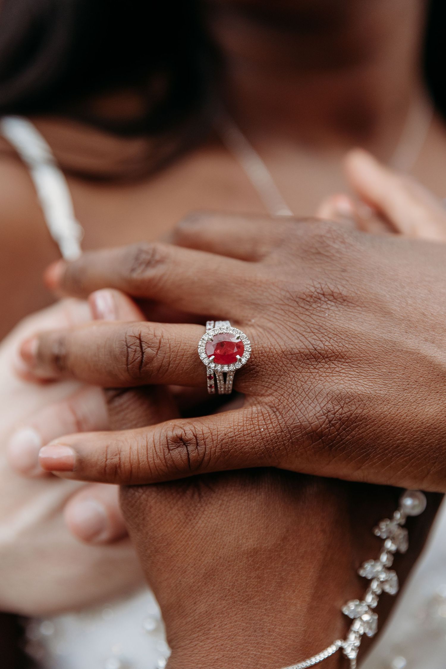 Close-up sequence of hands wearing a sparkling ruby and diamond halo engagement ring with wedding band.