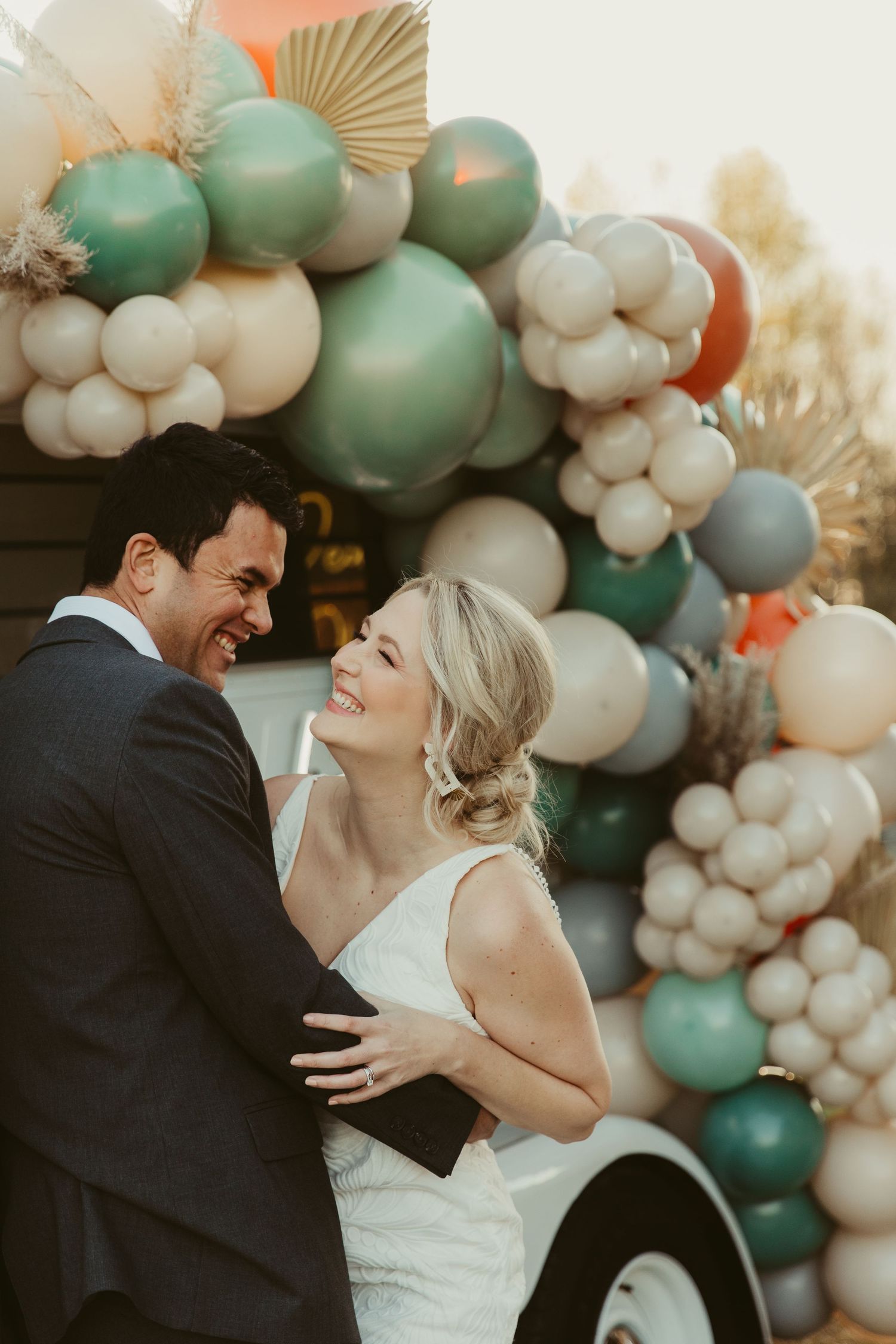 A couple shares a joyful moment together in front of an elegant balloon arch display in sage green and white colors.