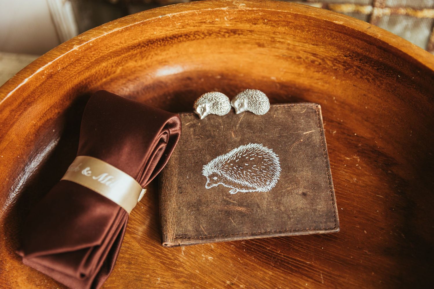 Groom details in a large wooden bowl. hedge hog wallet, shirt clips and a tie