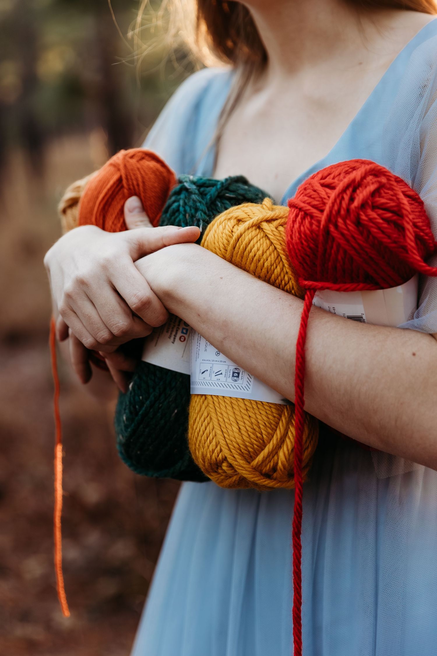Hands holding colorful yarn skeins in red, yellow, and dark green against a light blue dress background.