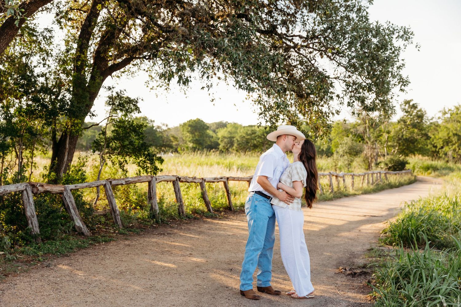 A couple in white and denim embrace and laugh together during a sunset photoshoot outdoors.