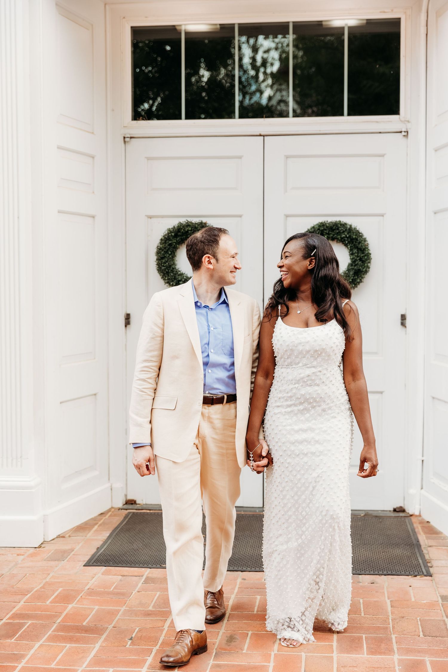 A couple in wedding attire shares joyful moments together on a white porch with terracotta tiles.