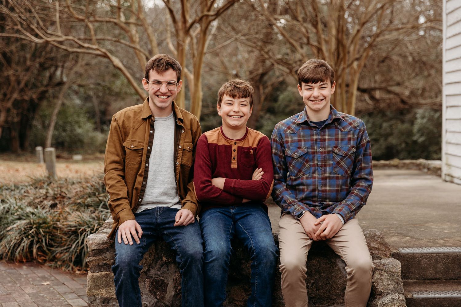 Three people wearing casual fall attire sit together on stone steps during an outdoor photo session.