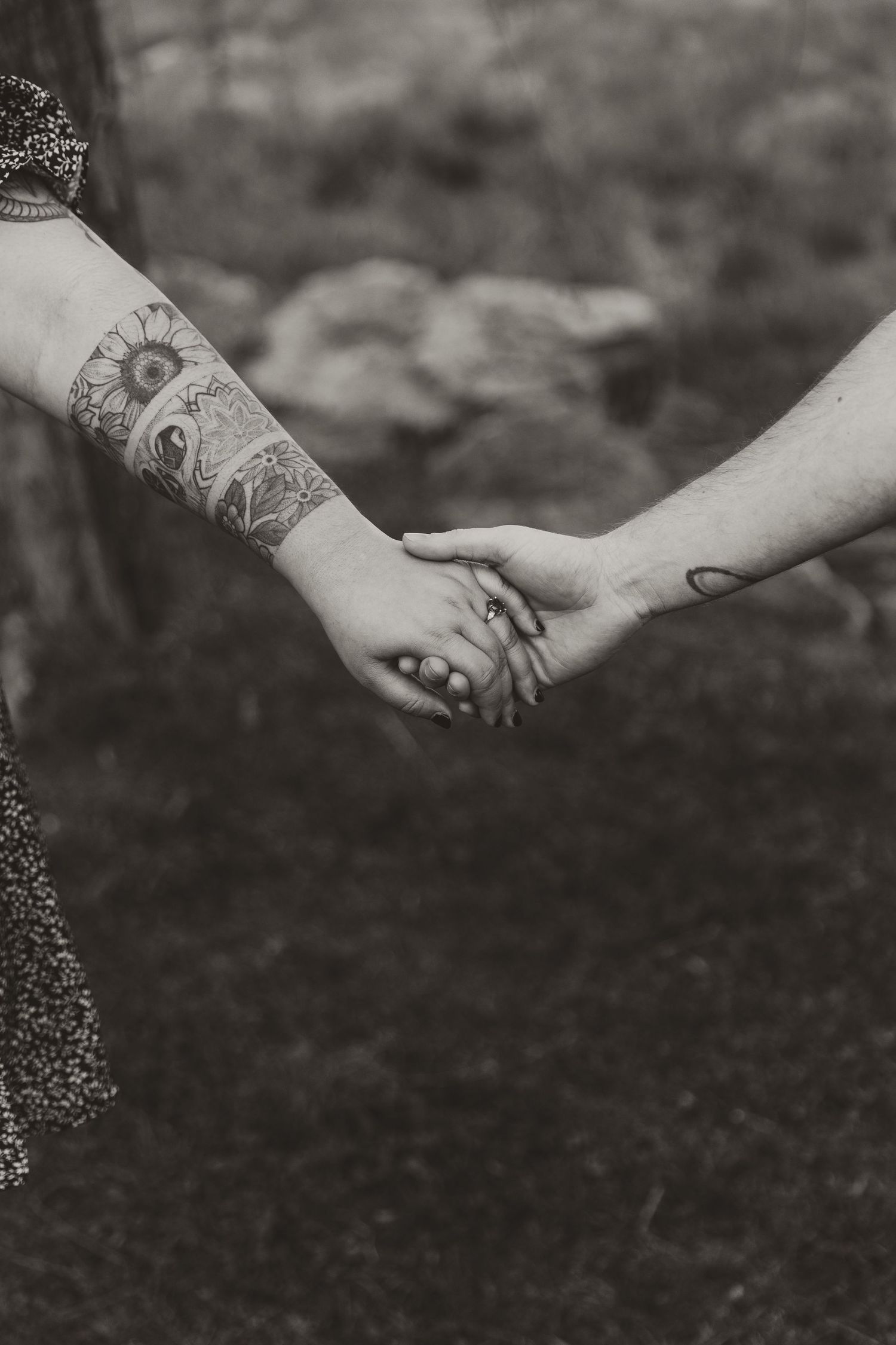 Black and white close-up of tattooed hands reaching towards each other against a dark blurred background.