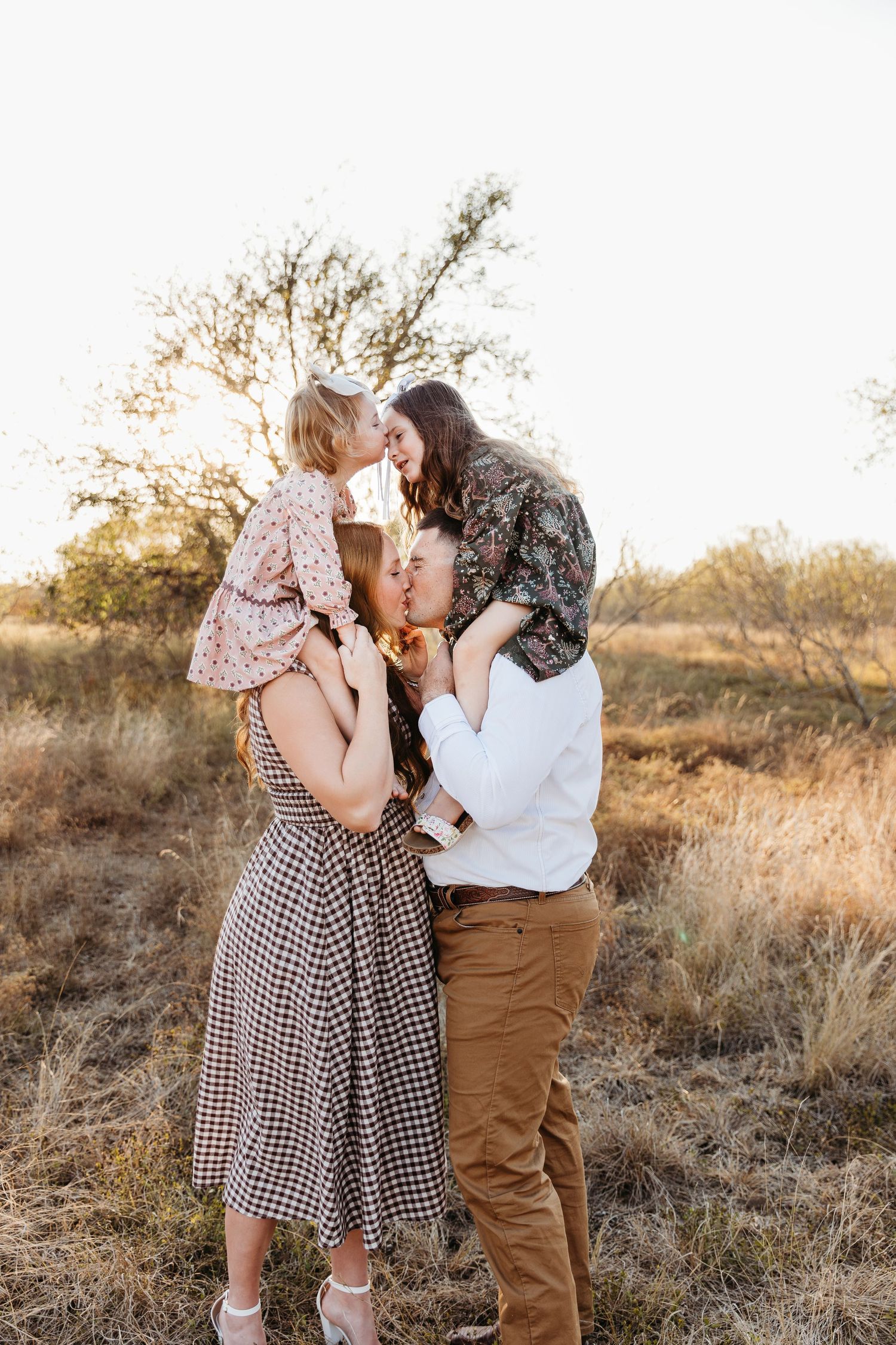 San Antonio family snuggling at crescent bend nature park. kids on piggy back and parents are kissing