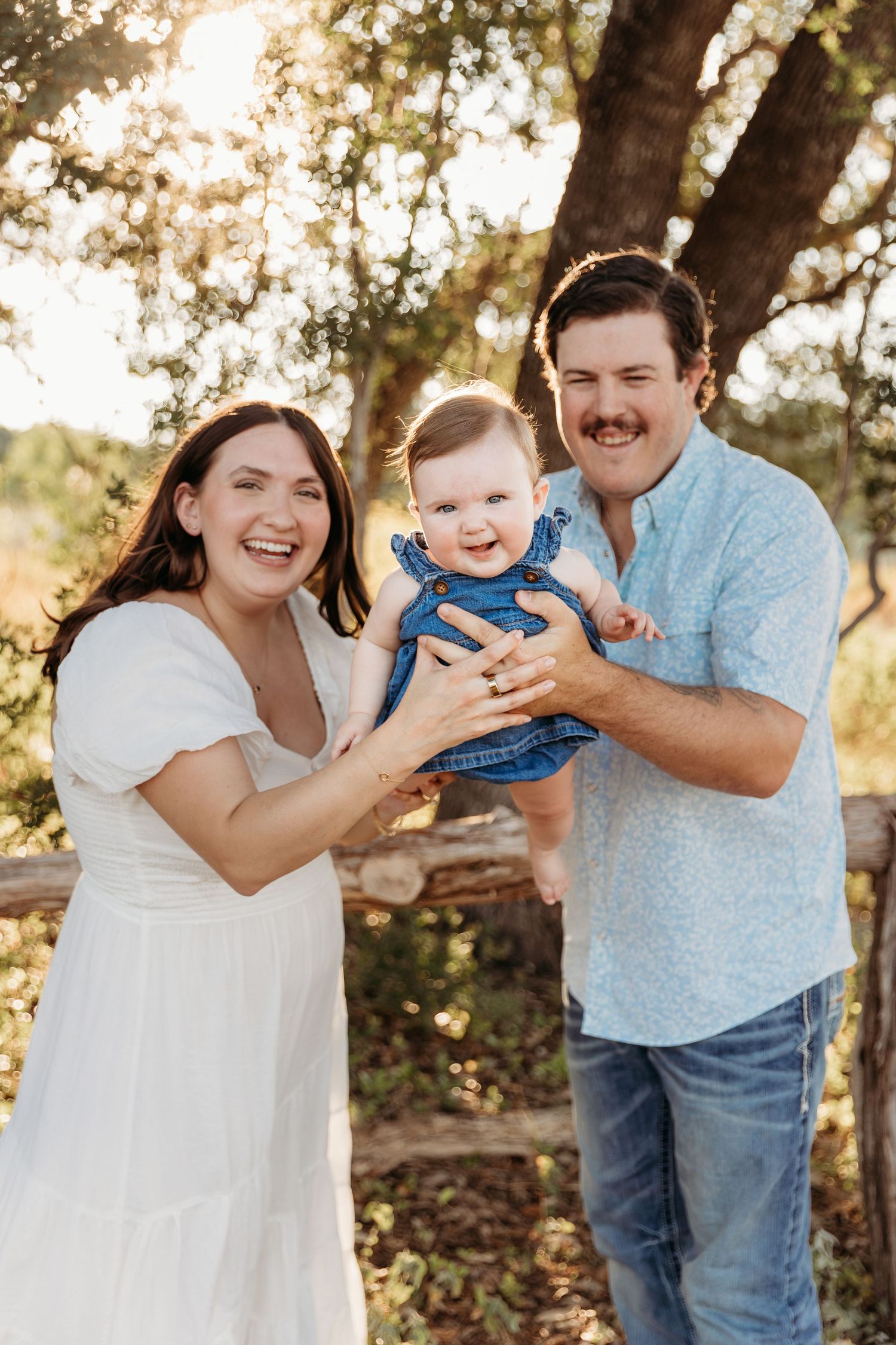 A family shares joyful moments together in a sun-dappled outdoor setting during a casual photo session.
